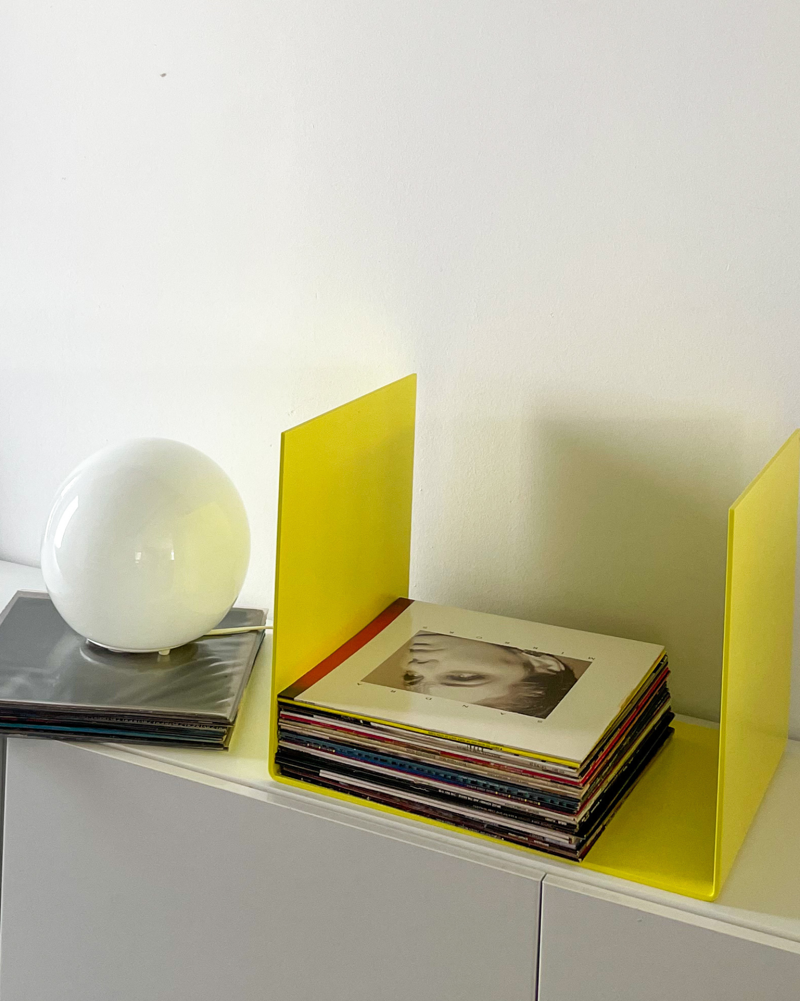 Nahaufnahme einer schwefelgelben Metallablage auf einer weißen Kommode, dekoriert mit Vinyl-Schallplatten und einem gerahmten Kunstobjekt, modernes Wohnaccessoire
