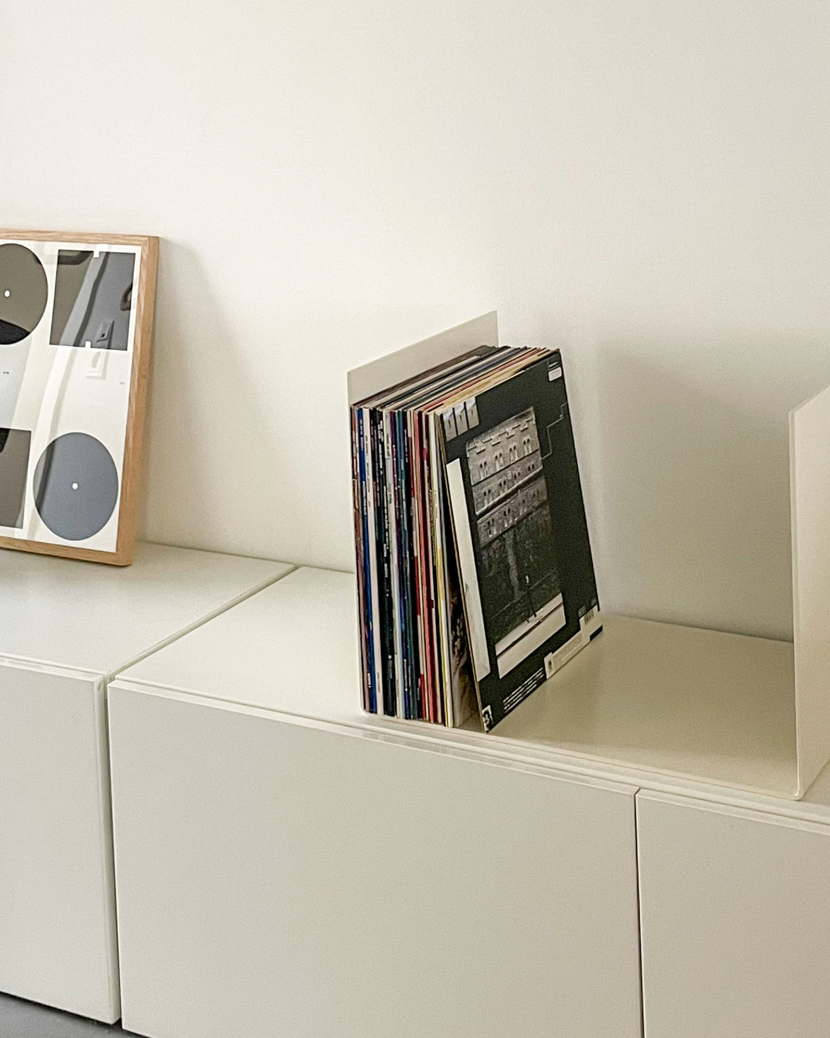 Nahaufnahme einer cremeweißen Metallablage auf einer weißen Kommode, dekoriert mit Vinyl-Schallplatten und einem gerahmten Kunstobjekt, modernes Wohnaccessoire