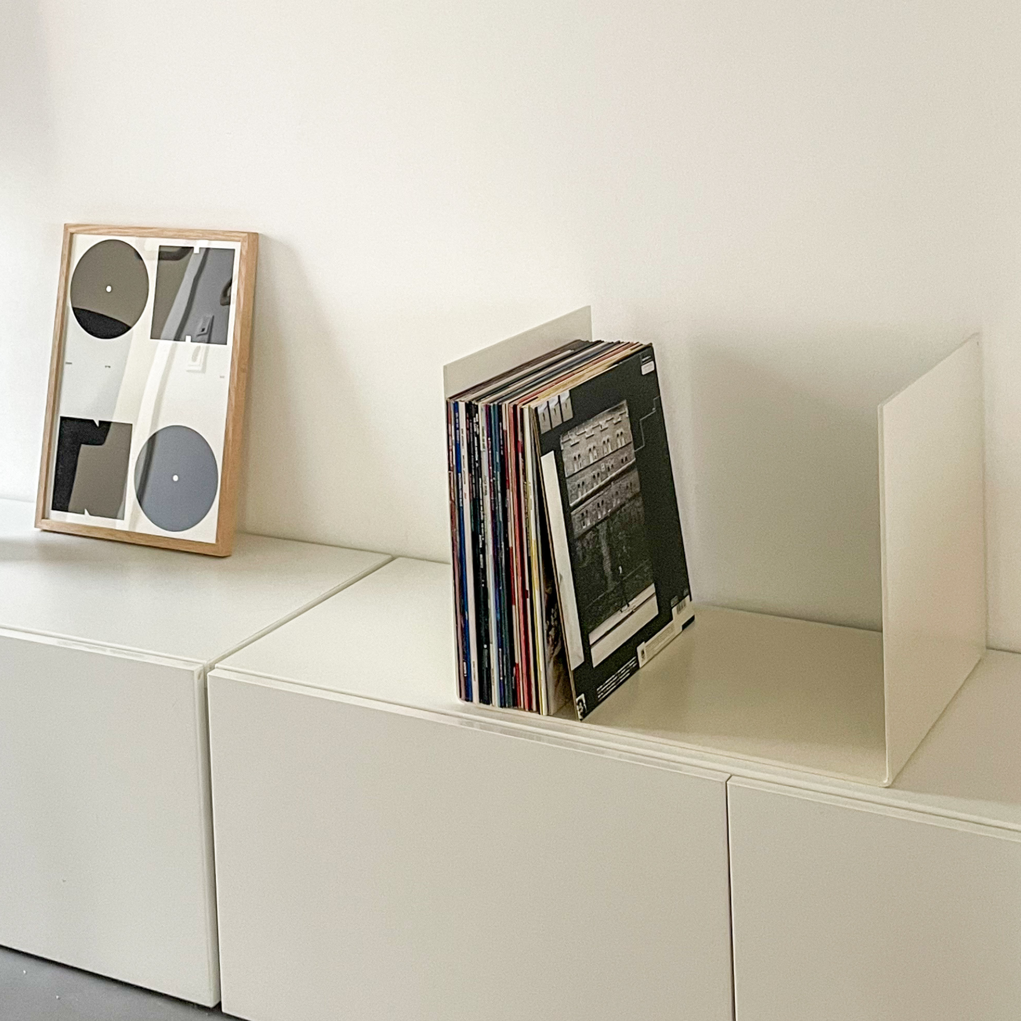 Nahaufnahme einer cremeweißen Metallablage auf einer weißen Kommode, dekoriert mit Vinyl-Schallplatten und einem gerahmten Kunstobjekt, modernes Wohnaccessoire