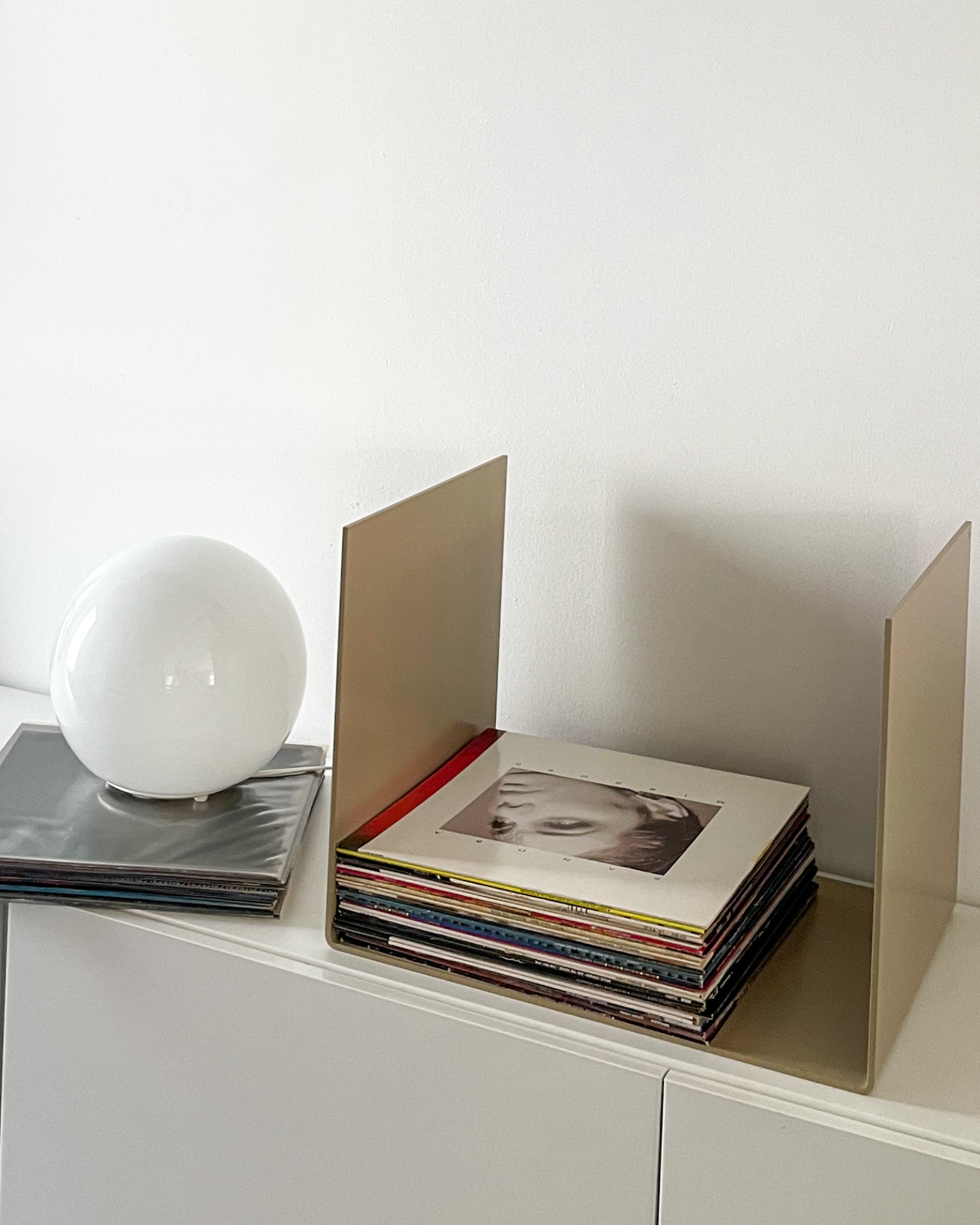 Nahaufnahme einer graubeigen Metallablage auf einer weißen Kommode, dekoriert mit Vinyl-Schallplatten und einem gerahmten Kunstobjekt, modernes Wohnaccessoire