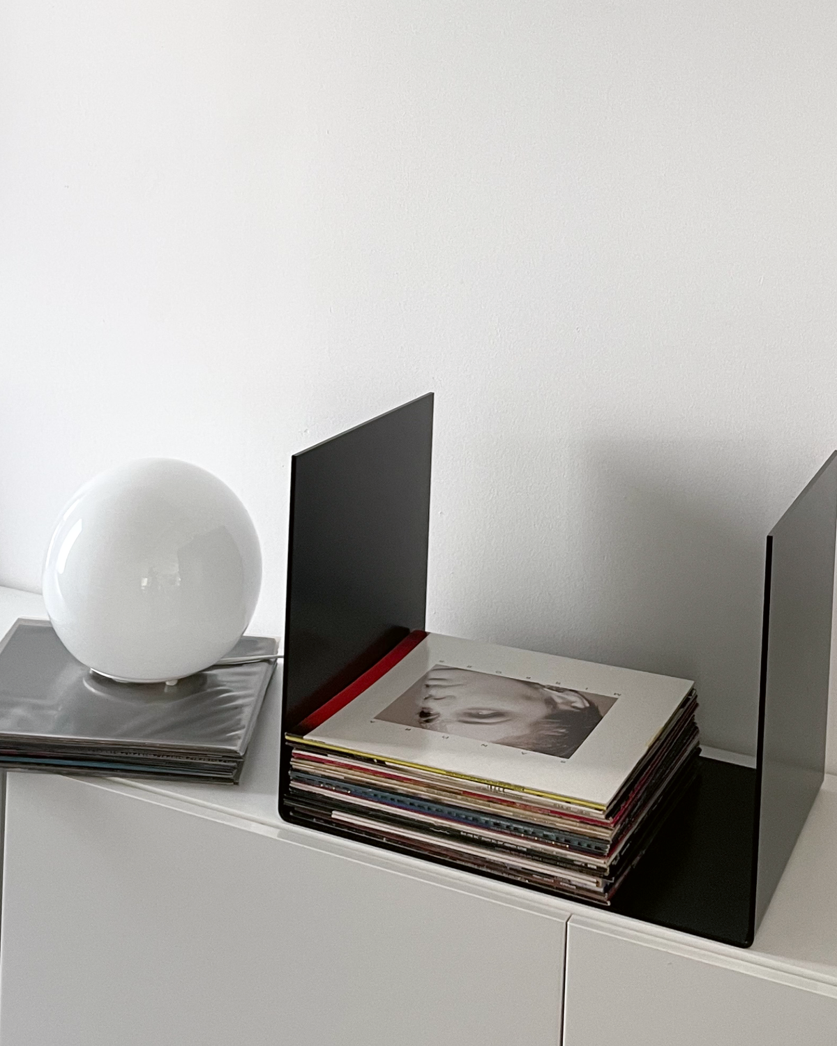 Nahaufnahme einer schwarzen Metallablage auf einer weißen Kommode, dekoriert mit Vinyl-Schallplatten und einem gerahmten Kunstobjekt, modernes Wohnaccessoire