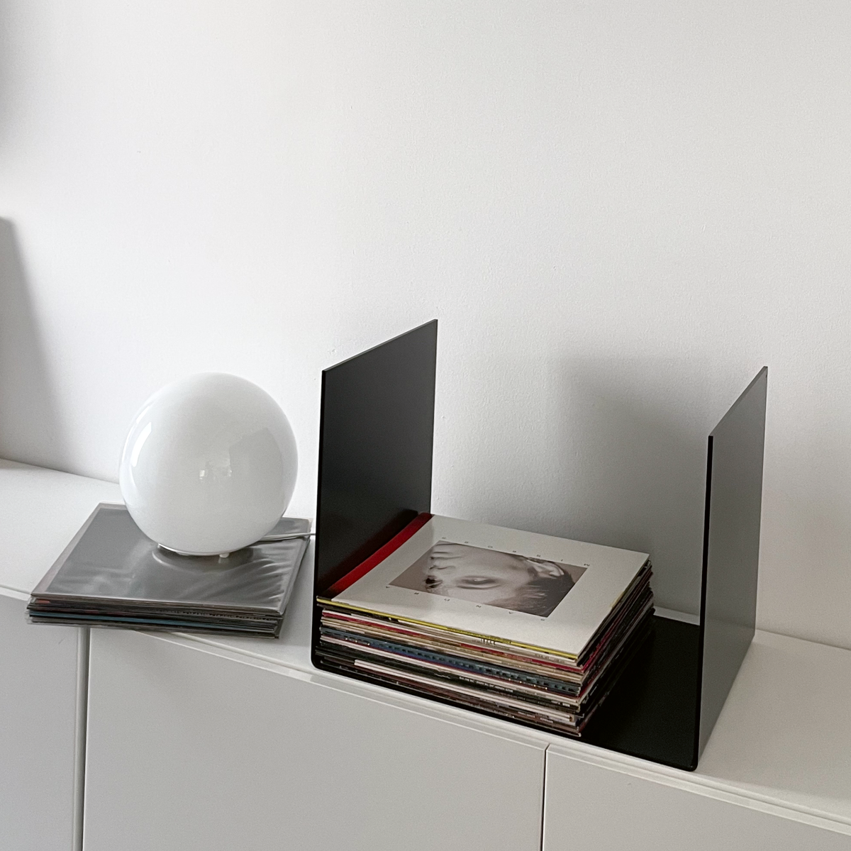 Nahaufnahme einer schwarzen Metallablage auf einer weißen Kommode, dekoriert mit Vinyl-Schallplatten und einem gerahmten Kunstobjekt, modernes Wohnaccessoire