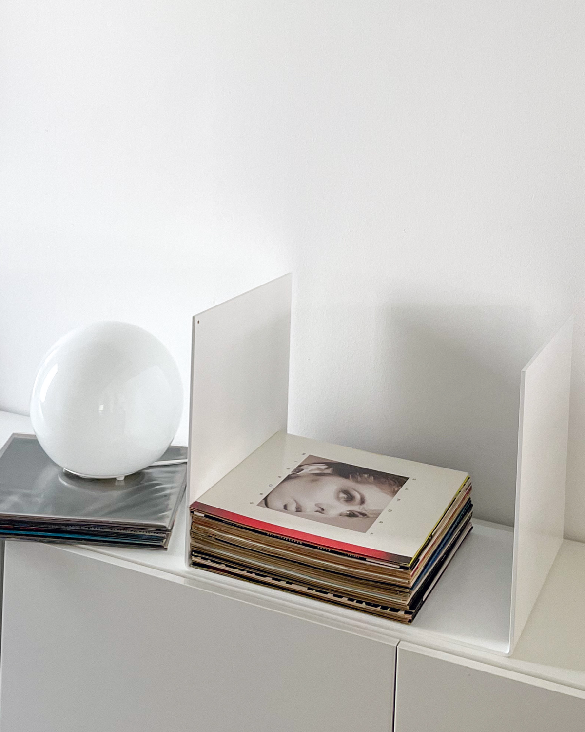 Nahaufnahme einer weißen Metallablage auf einer weißen Kommode, dekoriert mit Vinyl-Schallplatten und einem gerahmten Kunstobjekt, modernes Wohnaccessoire
