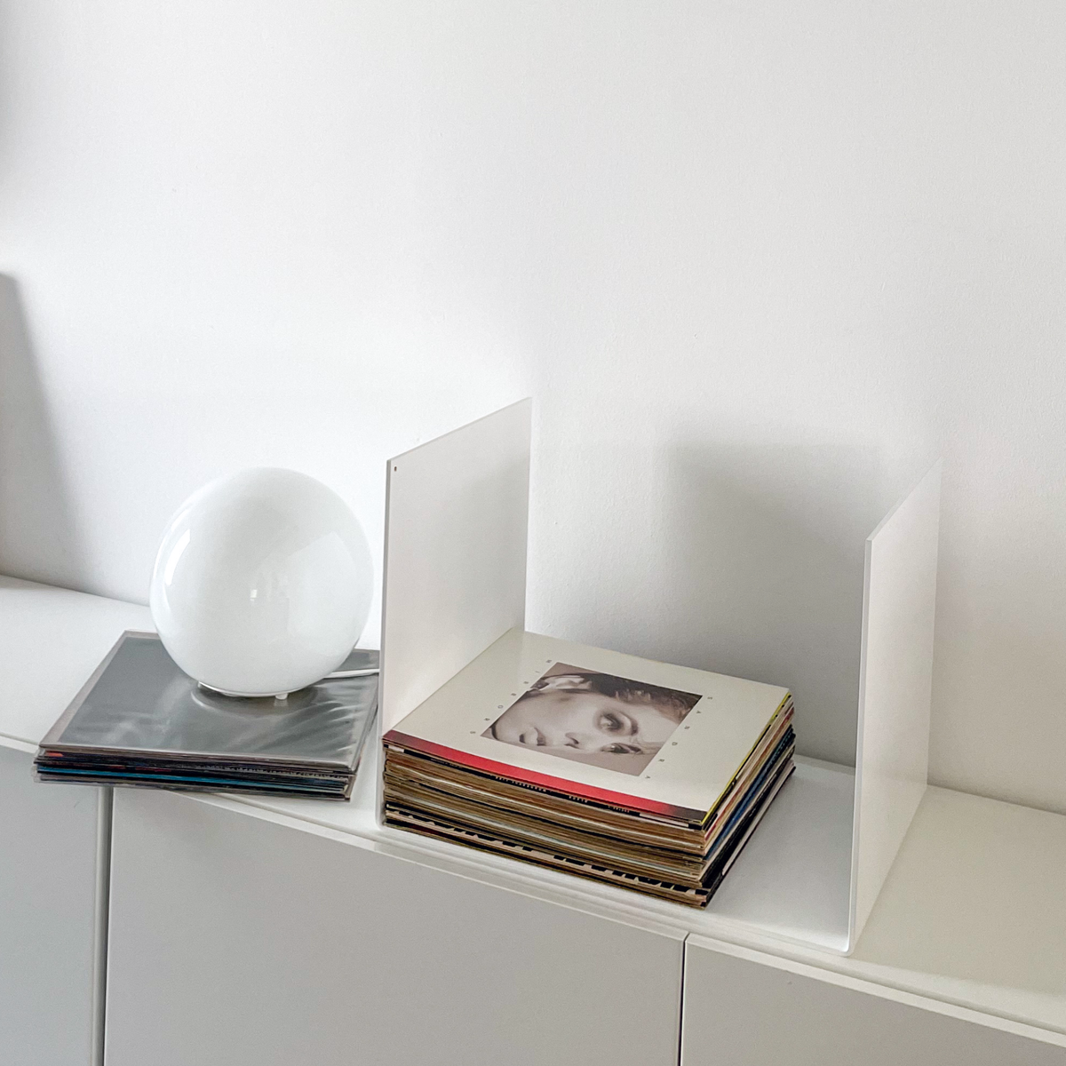 Nahaufnahme einer weißen Metallablage auf einer weißen Kommode, dekoriert mit Vinyl-Schallplatten und einem gerahmten Kunstobjekt, modernes Wohnaccessoire