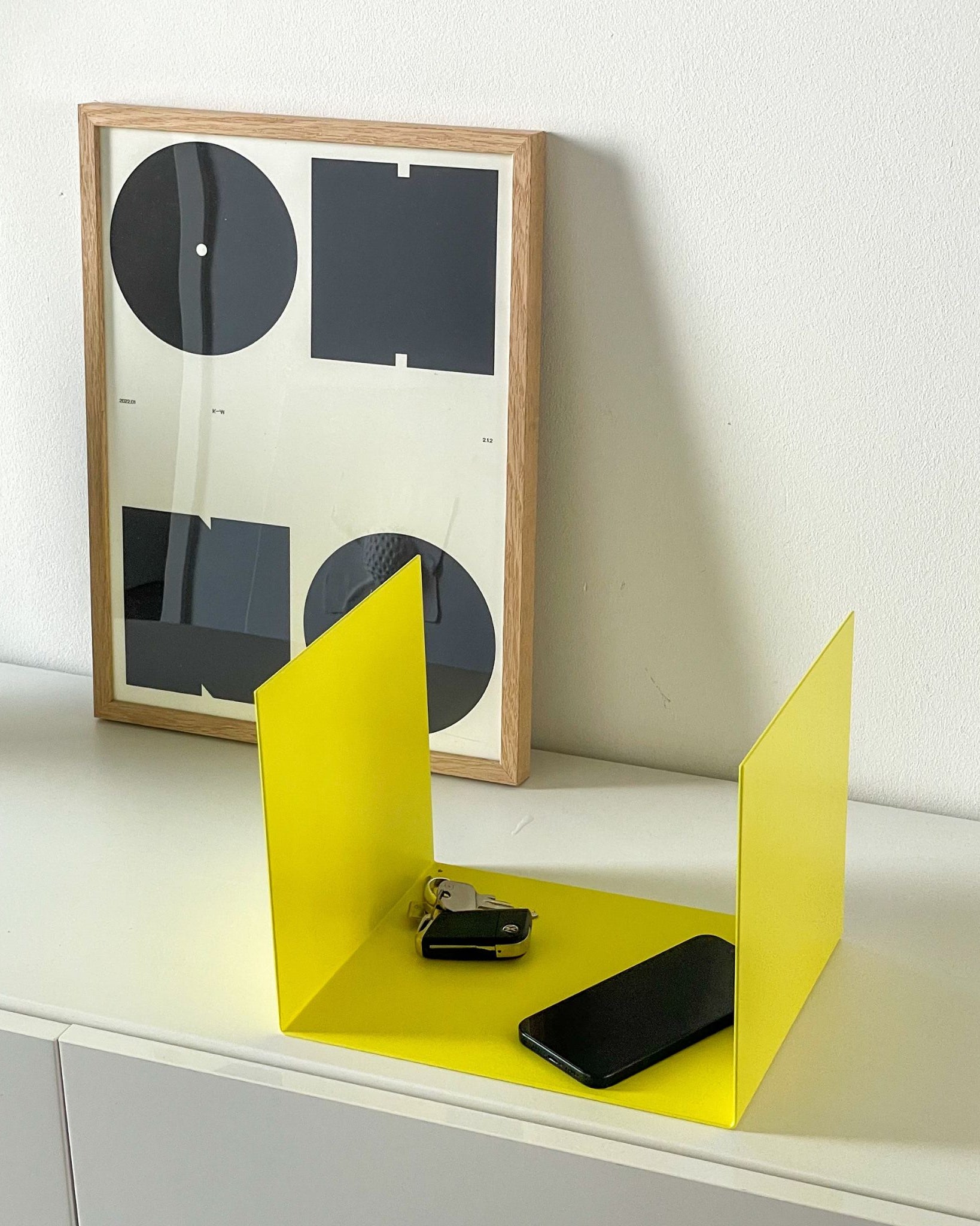 Kleine gelbe Ablage auf einer Kommode im Flur, dekoriert mit einem Bildrahmen, Smartphone und Schlüsseln