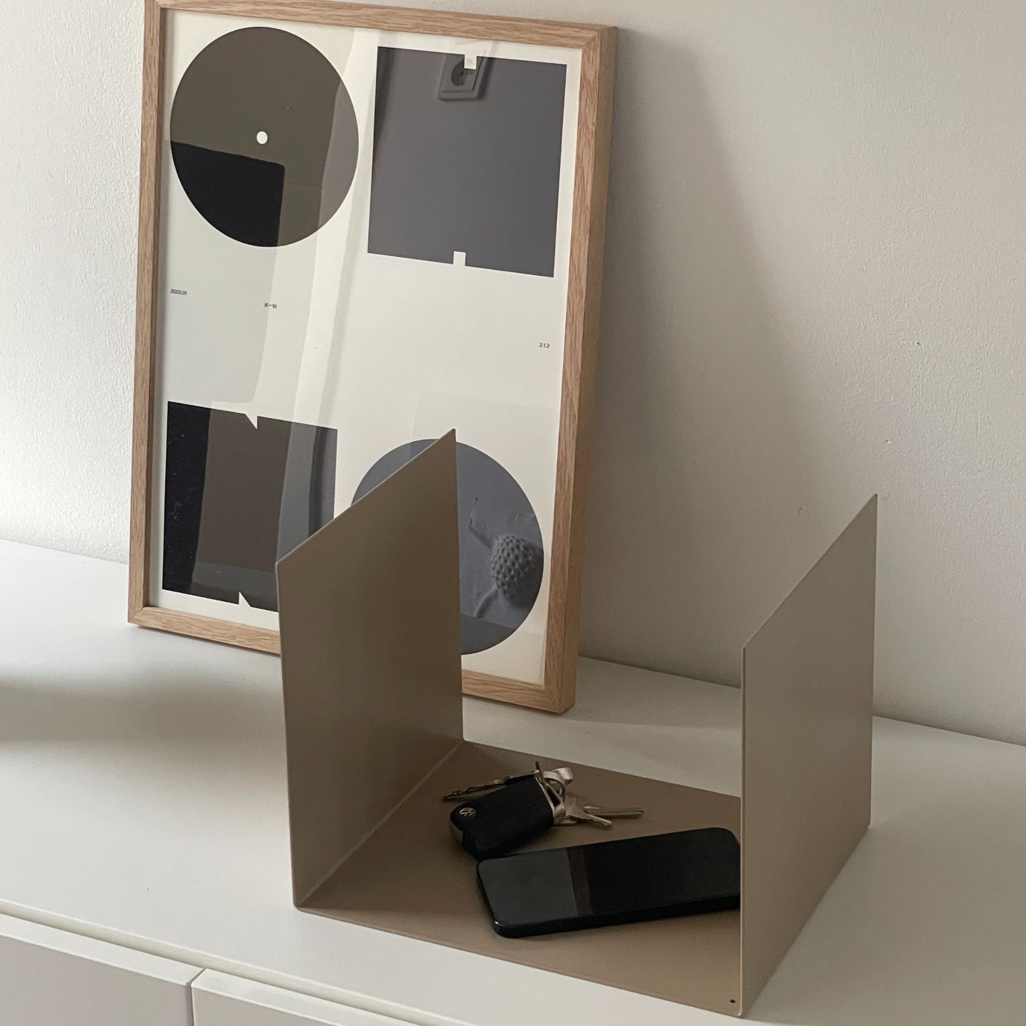 Kleine graubeiges Ablage auf einer weißen Kommode, dekoriert mit einem Bilderrahmen, Schlüssel und Smartphone, modernes Wohnaccessoire