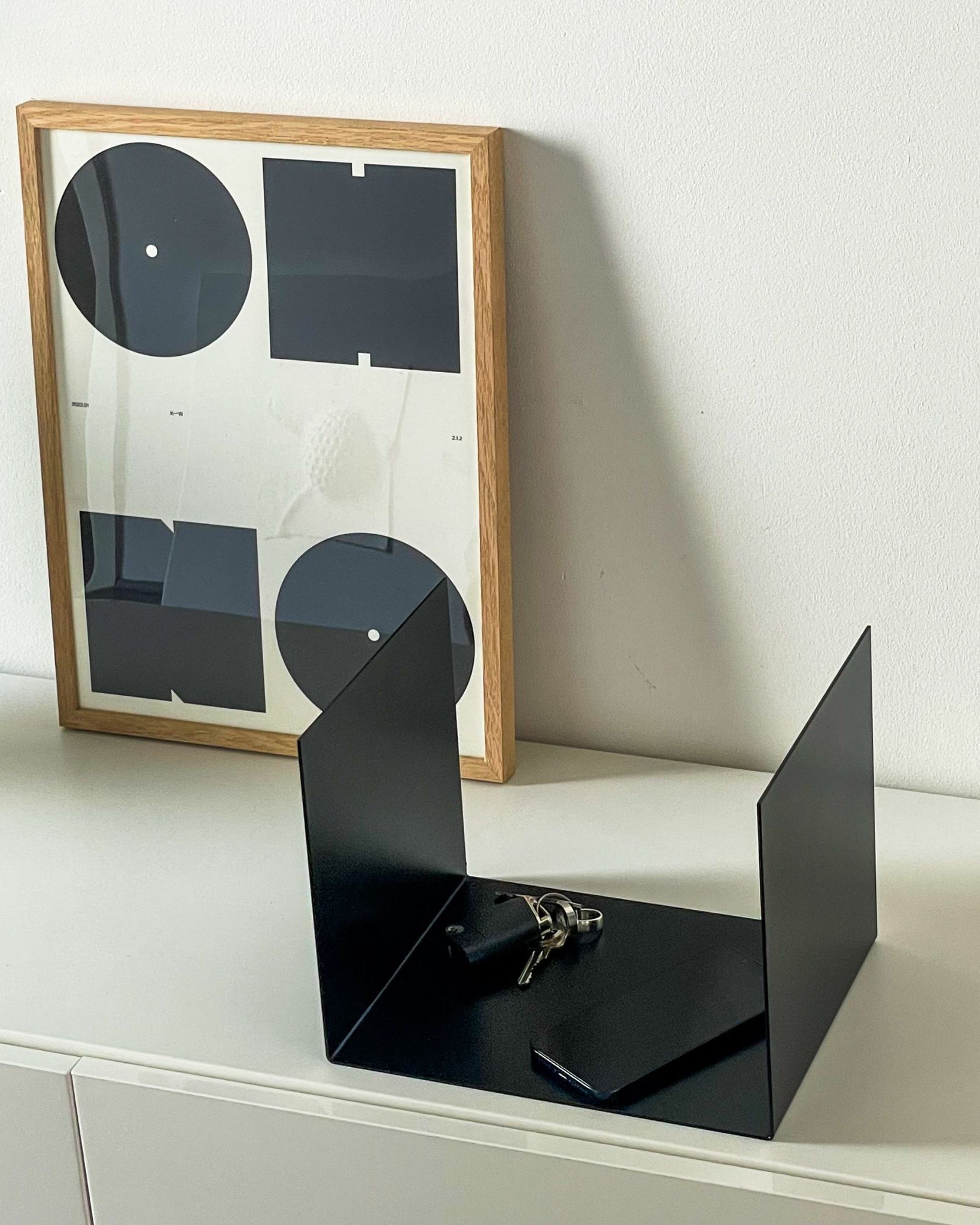 Kleine schwarze Ablage auf einer Kommode im Flur, dekoriert mit einem Bildrahmen, Smartphone und Schlüsseln