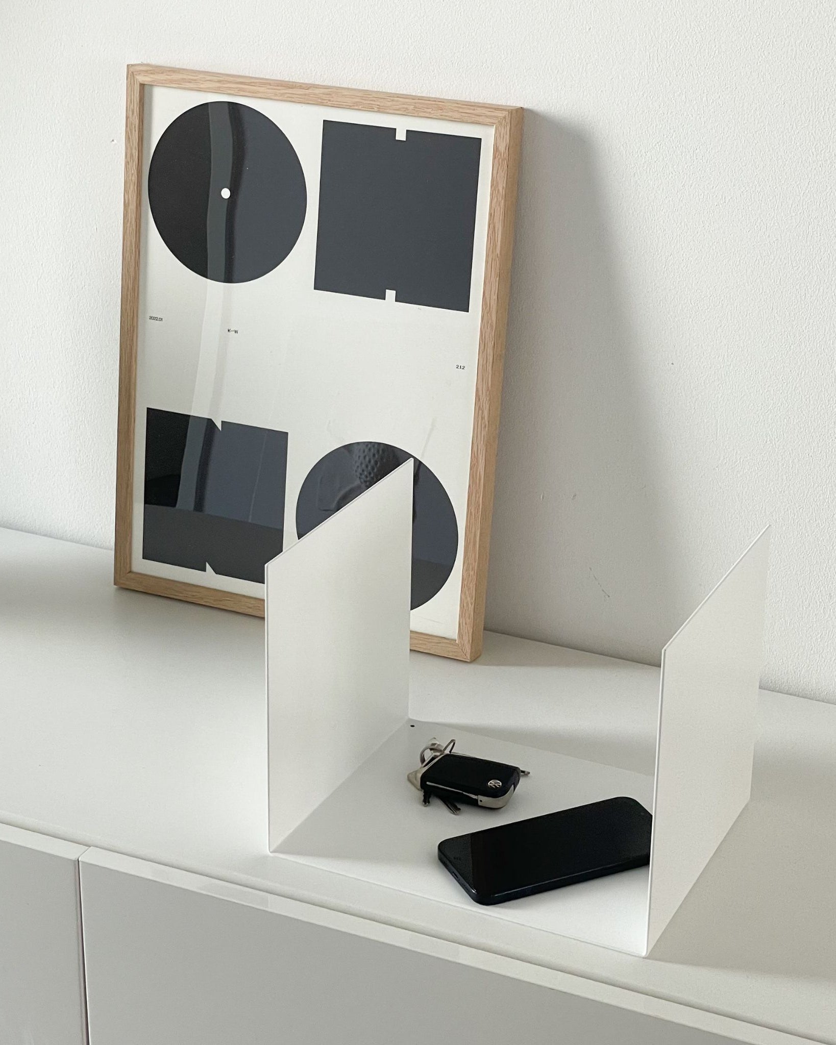 Kleine weiße Ablage auf einer Kommode im Flur, dekoriert mit einem Bildrahmen, Smartphone und Schlüsseln