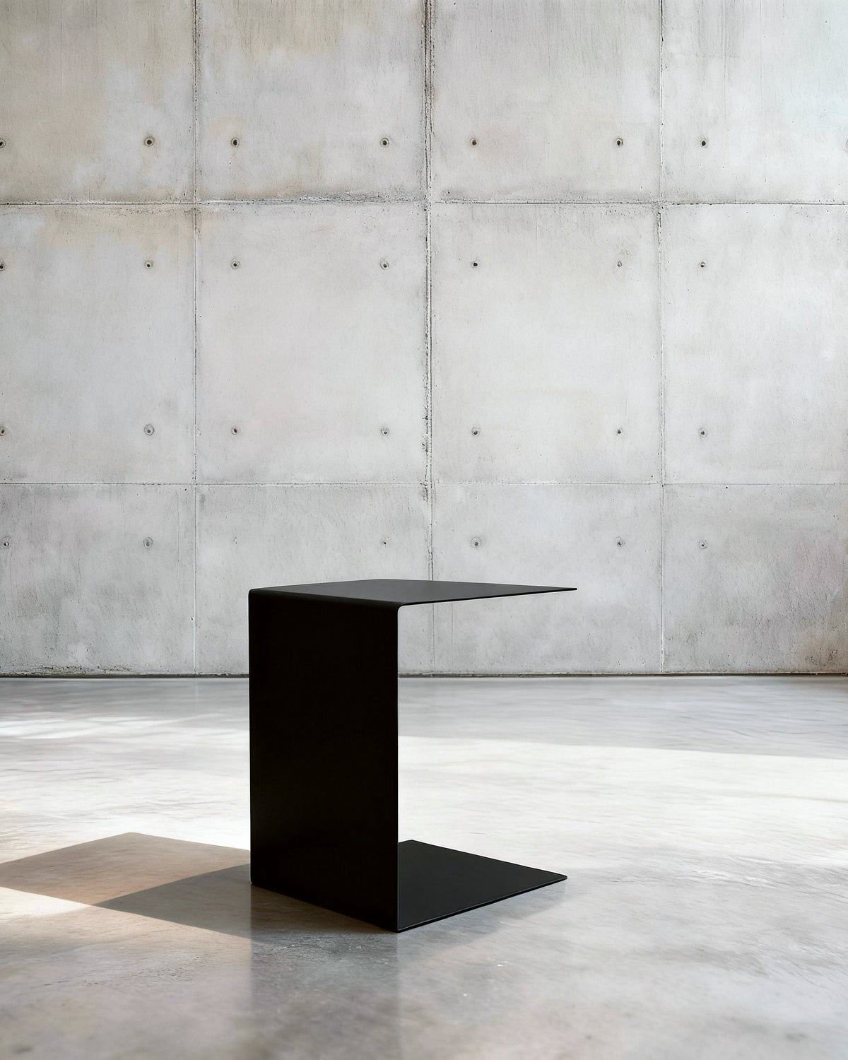 Minimalistischer Beistelltisch BIG C aus schwarz matt lackiertem Stahl in architektonischem Raum auf Betonboden