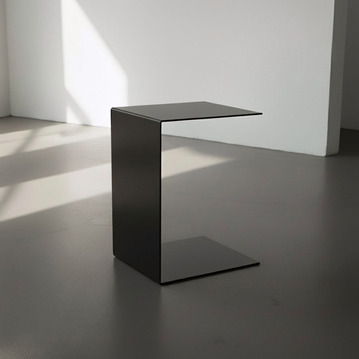 BIG C in schwarz auf grauen Betonboden vor weißer Wand und Lichtspiel