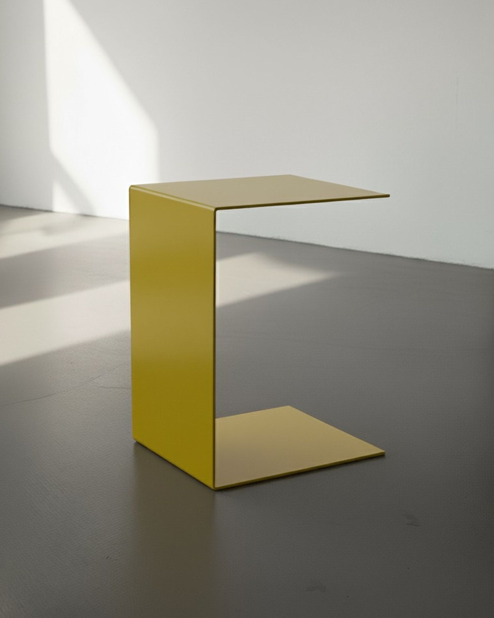 BIG C in schwefelgelb auf grauen Betonboden vor weißer Wand und Lichtspiel