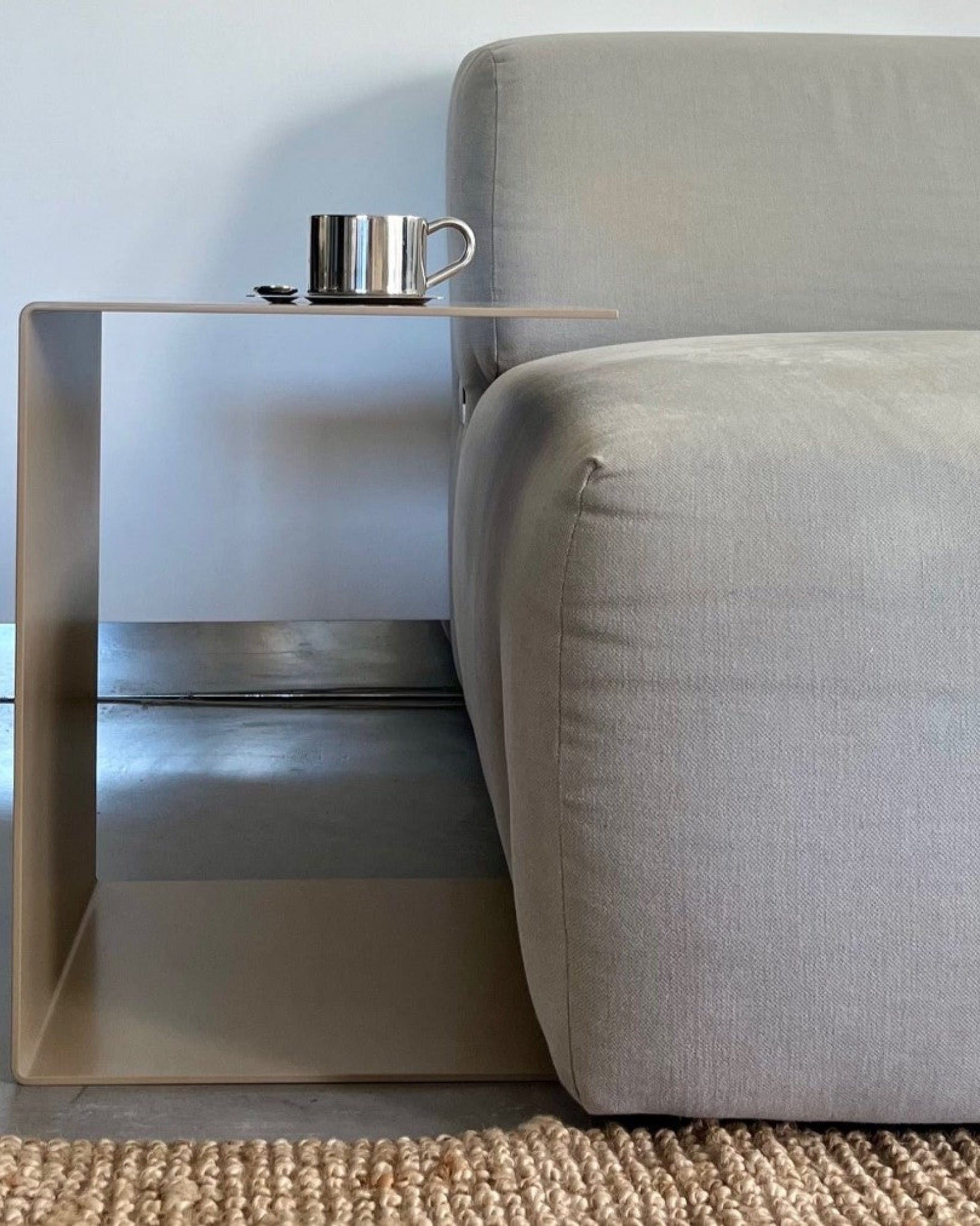 Graubeiger C-förmiger Beistelltisch neben einem grauen Sofa