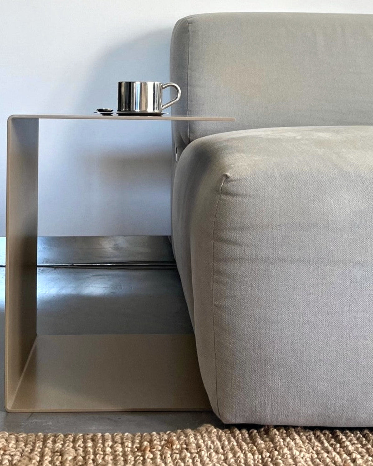 Graubeiger C-förmiger Beistelltisch neben einem grauen Sofa