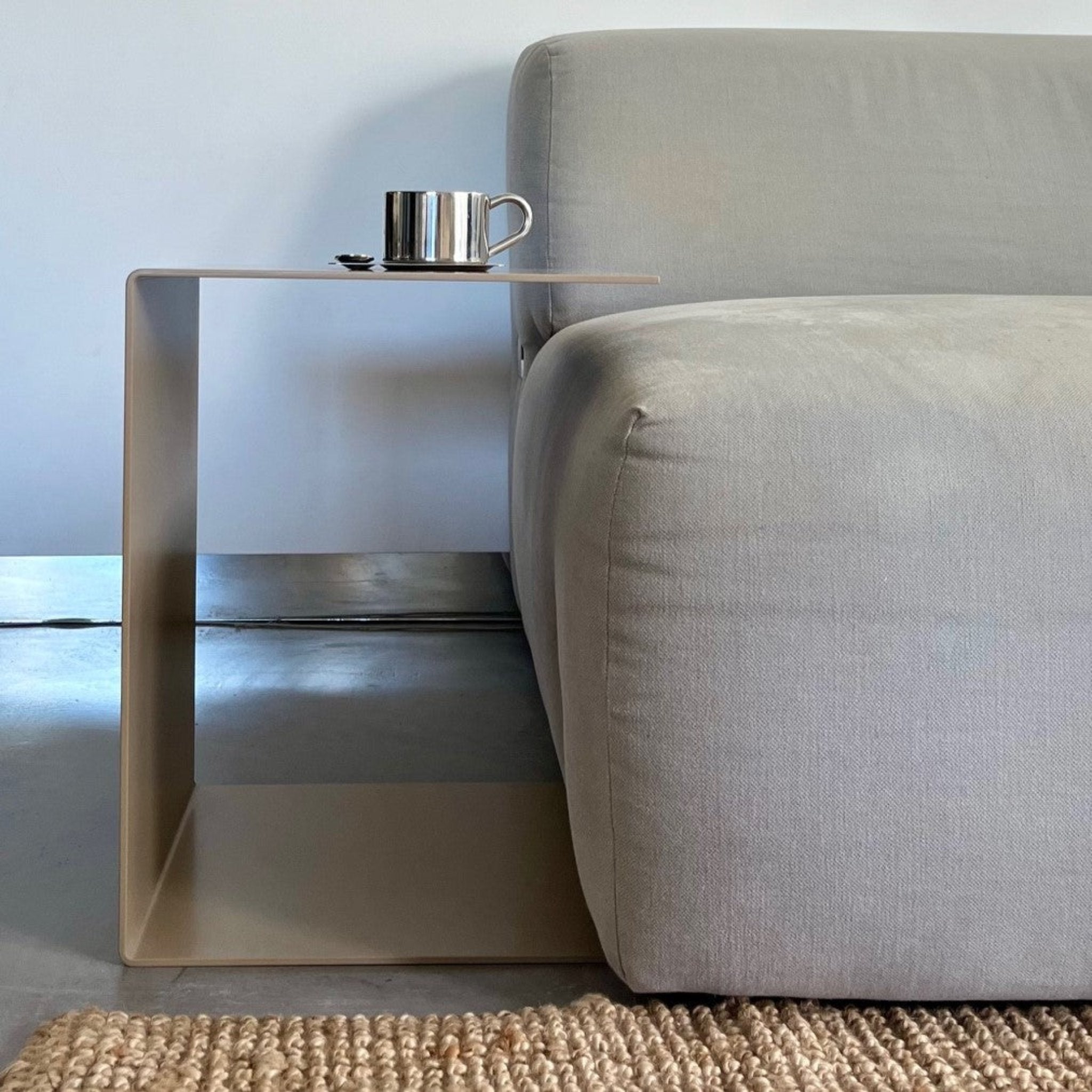 Graubeiger C-förmiger Beistelltisch neben einem grauen Sofa