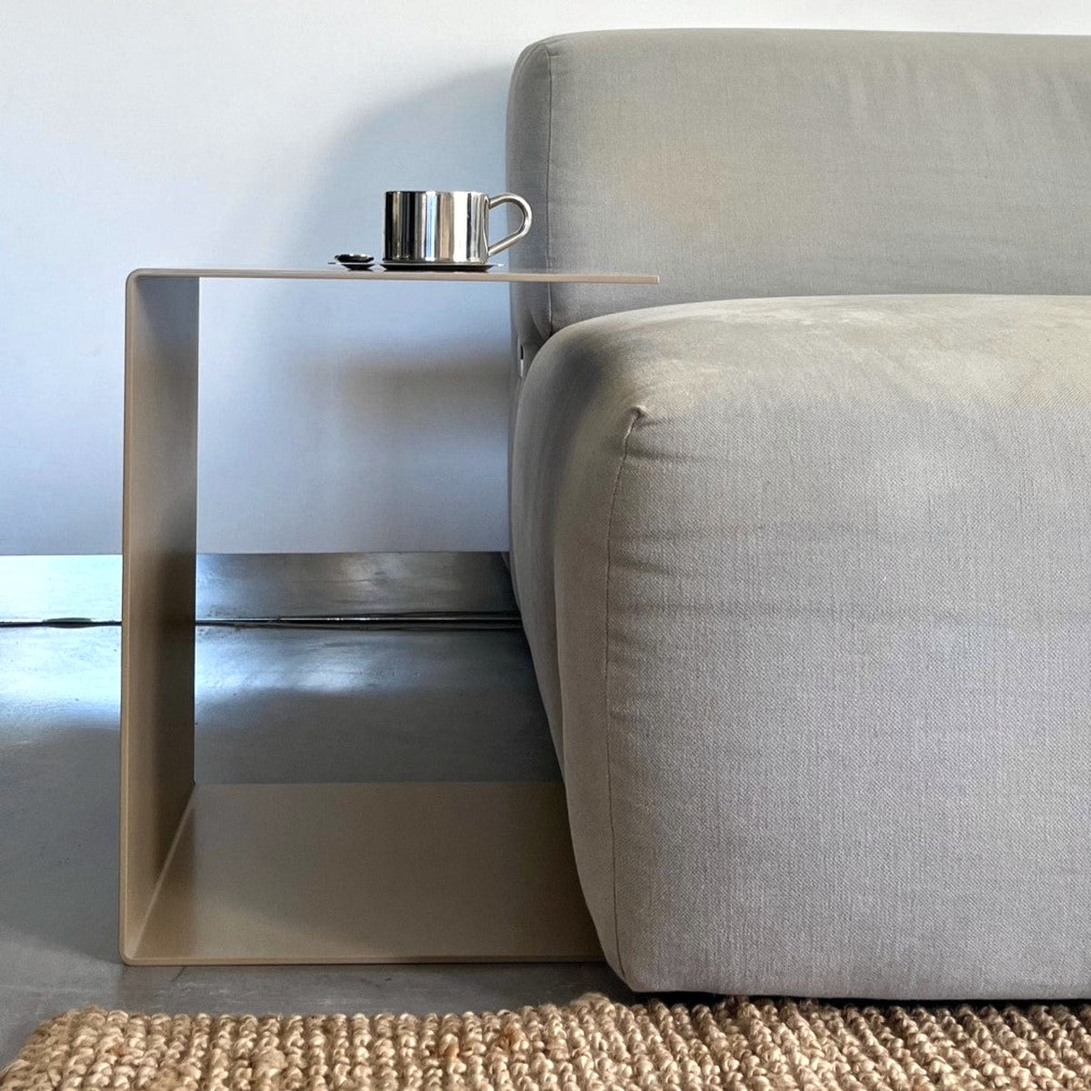 Graubeiger C-förmiger Beistelltisch neben einem grauen Sofa
