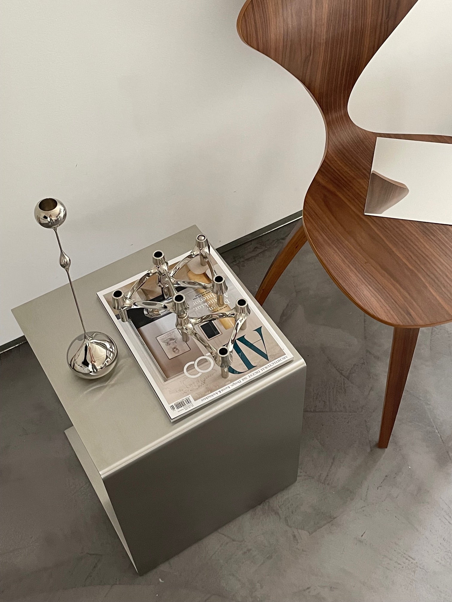 Beistelltisch aus gebürstetem Edelstahl mit Dekoration und Magazin neben einem Designer-Holzstuhl