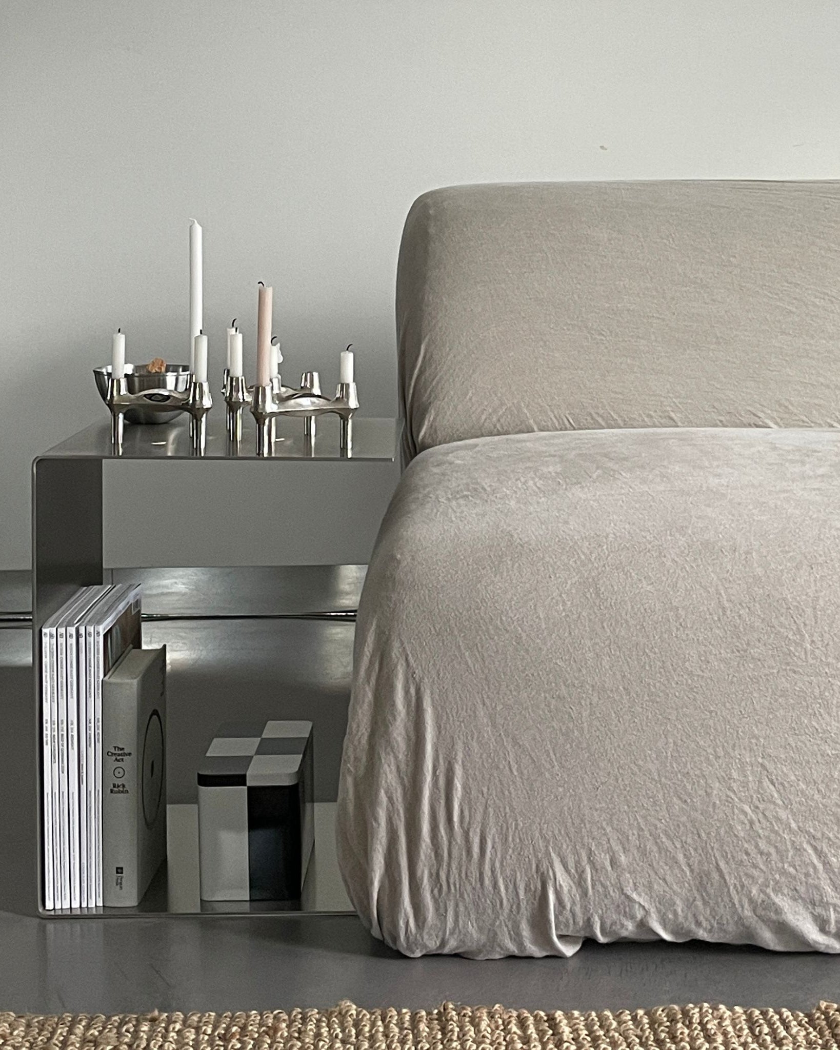 Minimalistischer Beistelltisch aus gebürstetem Edelstahl neben einem Sofa, dekoriert mit Kerzenhaltern und Magazinen