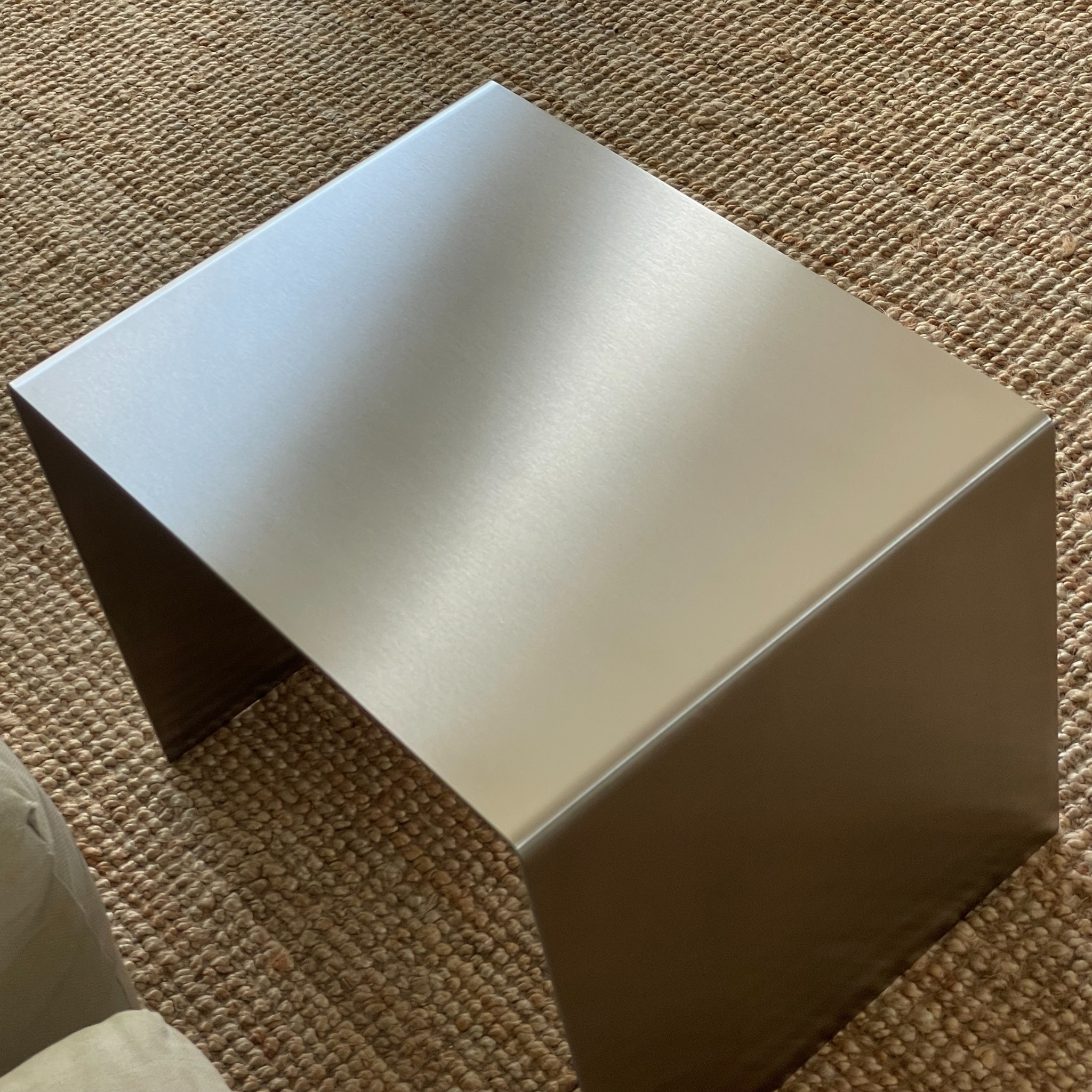 Quadratischer Beistelltisch aus gebürstetem Edelstahl auf einem Teppich im Wohnzimmer