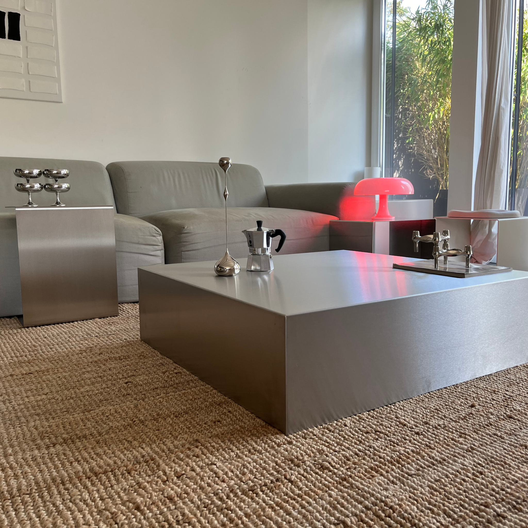 Wohnzimmer mit modernem quadratischem Couchtisch und Beistelltisch aus gebürstetem Edelstahl, grauem Sofa und roter Tischlampe