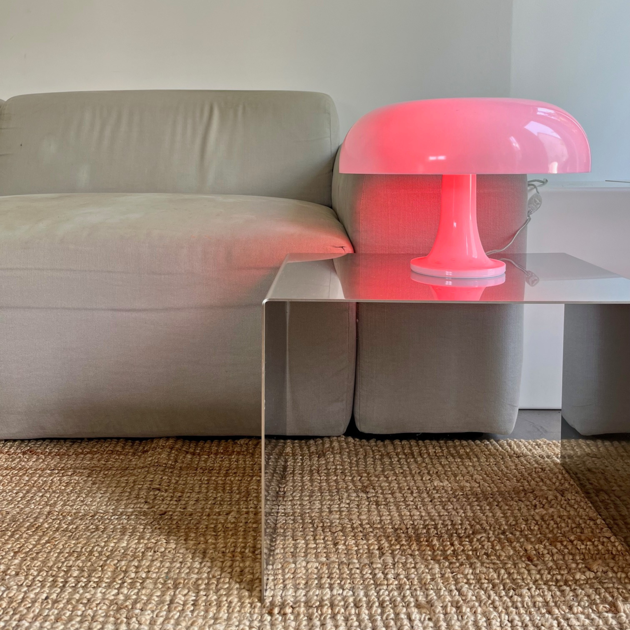 Moderner quadratischer Couchtisch aus gebürstetem Edelstahl mit roter Design-Tischlampe vor einem grauen Sofa im Wohnzimmer