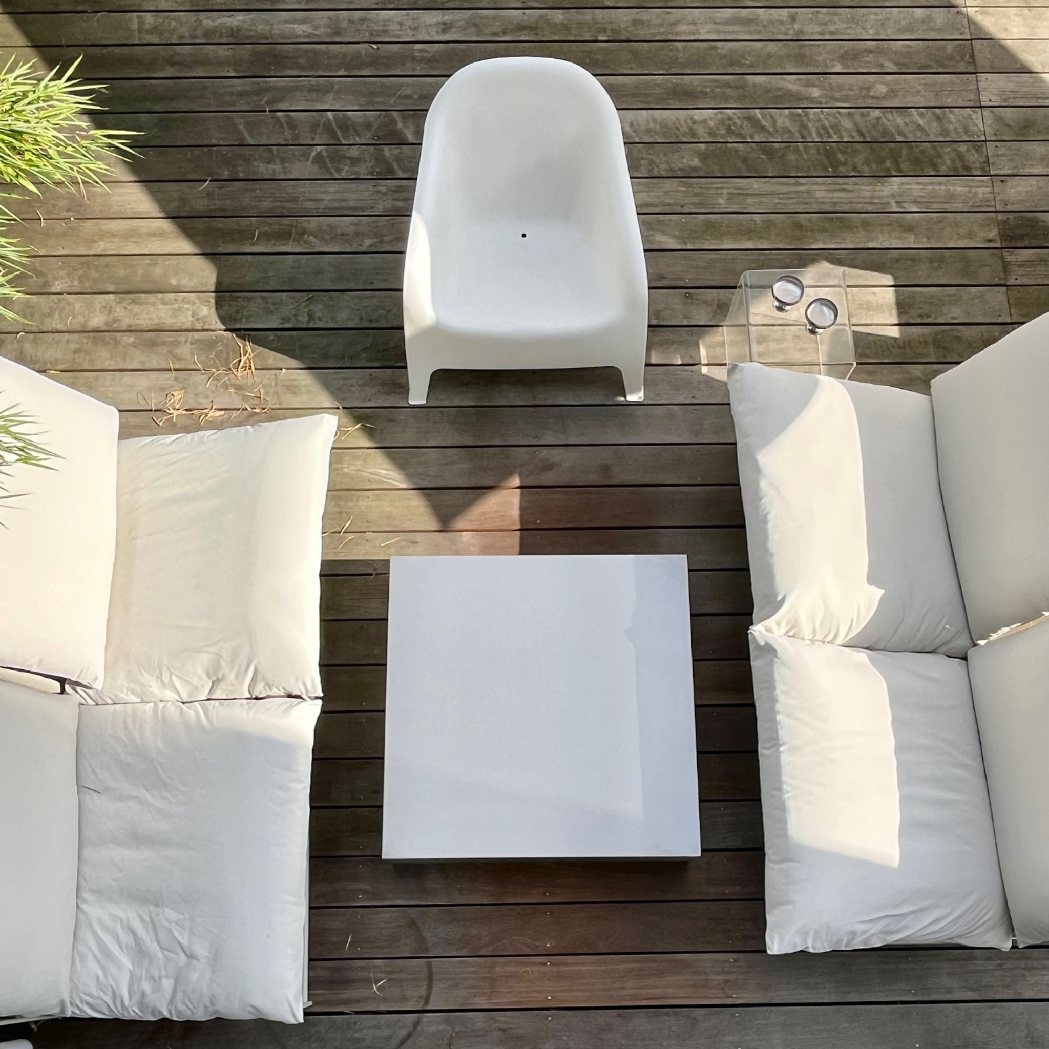 MO INTERIORS Outdoor-Lounge mit quadratischem Couchtisch aus gebürstetem Edelstahl auf Holzterrasse, umgeben von weißen Sofas und einem modernen weißen Sessel – stilvolles und minimalistisches Terrassendesign.
