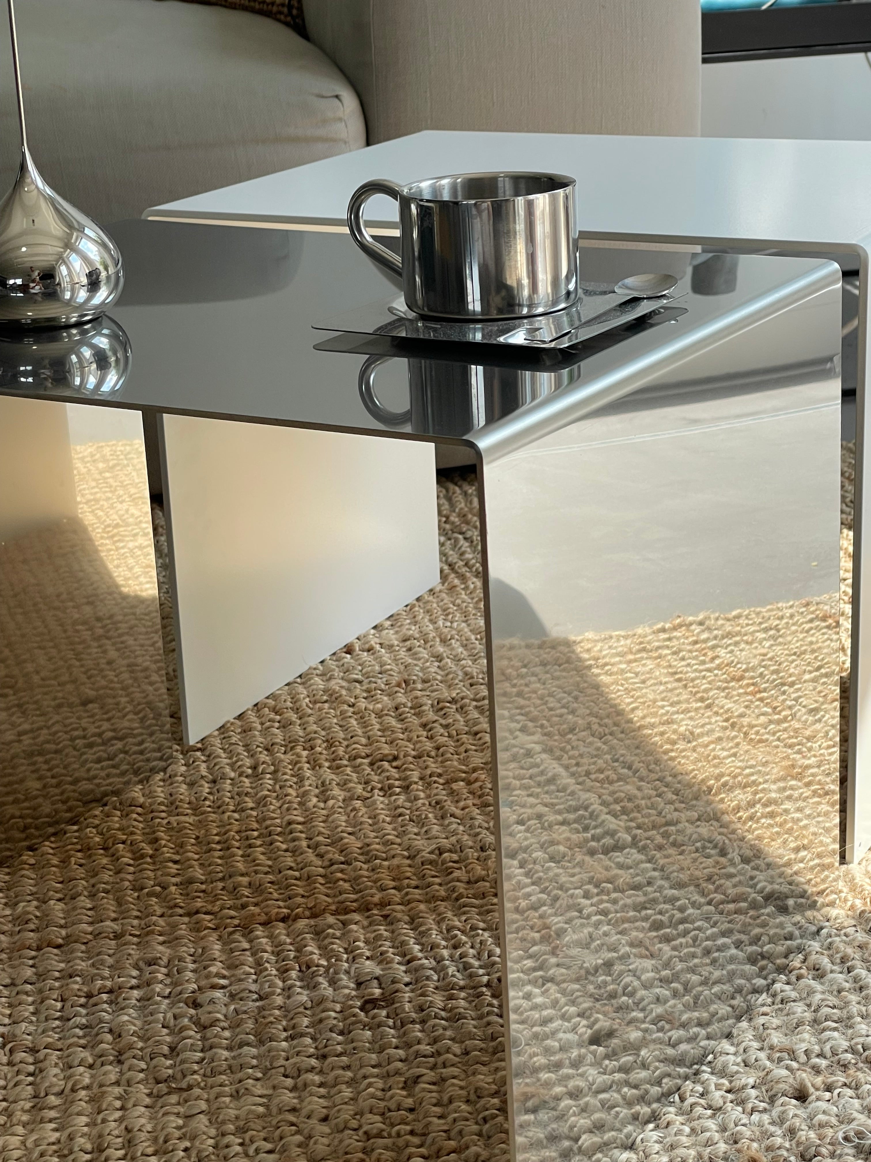 MO INTERIORS spiegelpolierter Couchtisch, dekoriert mit einer silbernen Tasse und einer eleganten Skulptur, in einem modernen Wohnzimmer auf strukturiertem Teppich – minimalistisches Design.