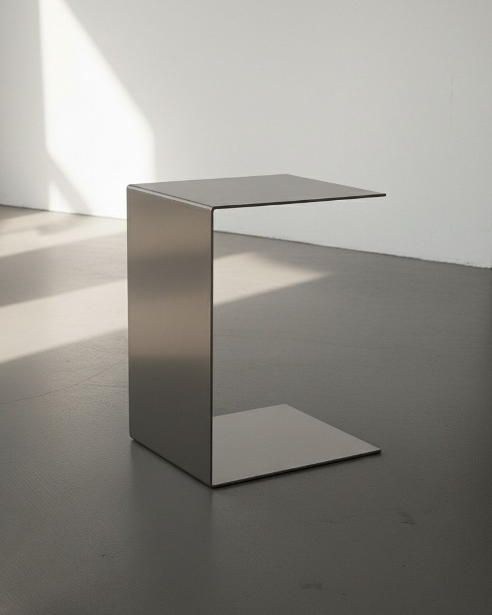 Brushed C aus Edelstahl gebürstet auf grauen Betonboden vor weißer Wand und Lichtspiel