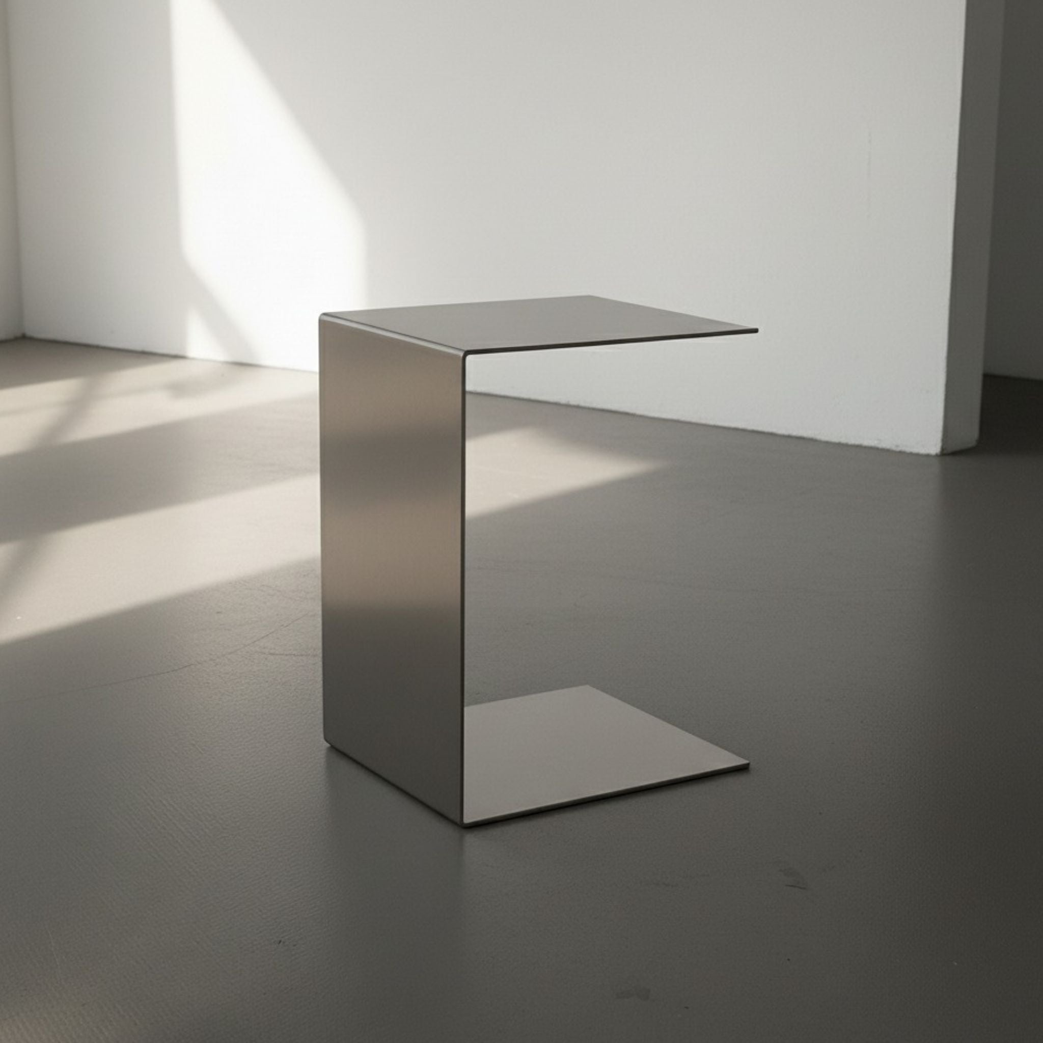 Brushed C aus Edelstahl gebürstet auf grauen Betonboden vor weißer Wand und Lichtspiel