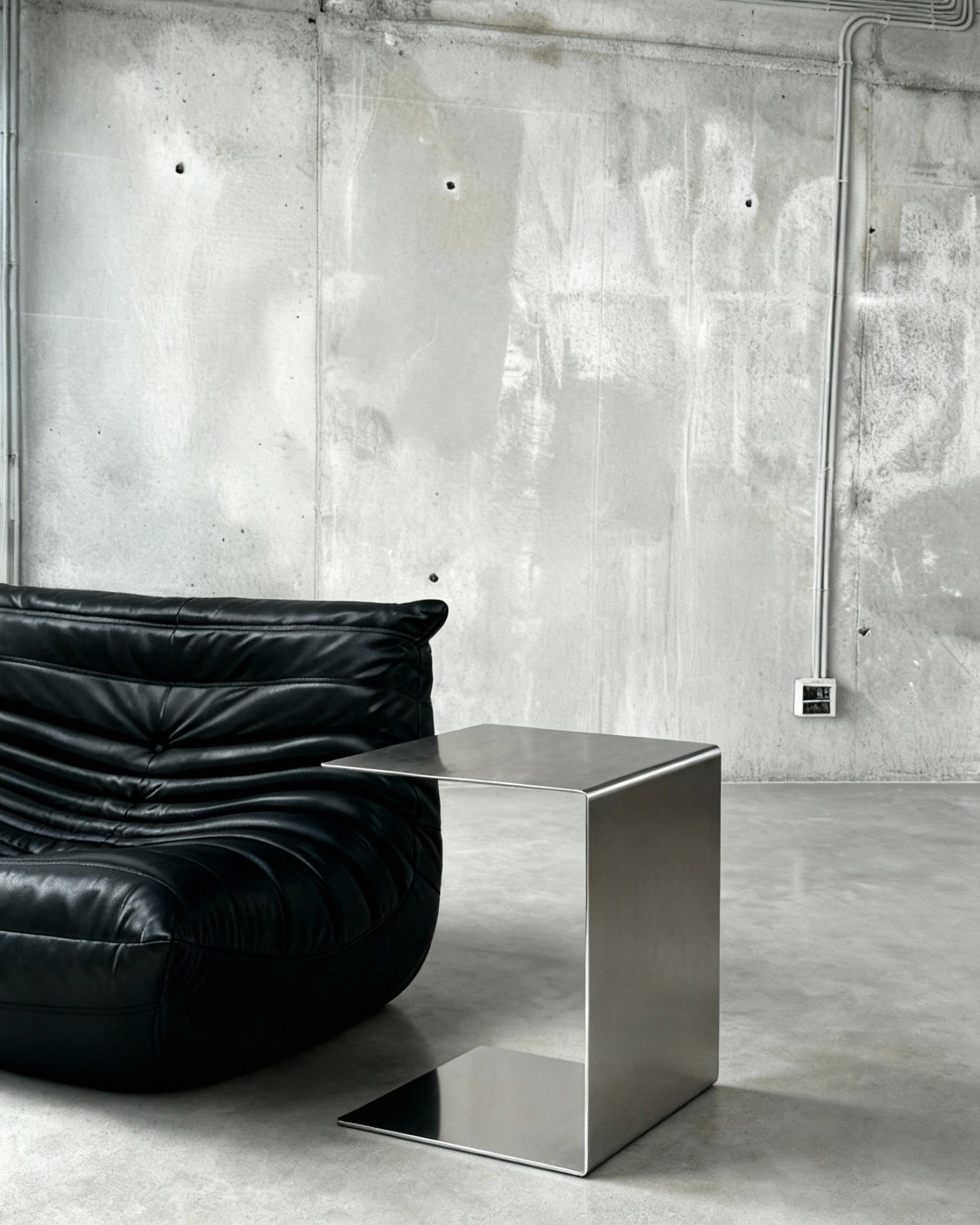 Brushed C vor Betonwand auf Betonboden mit schwarzem lignet rose Sofa aus Leder