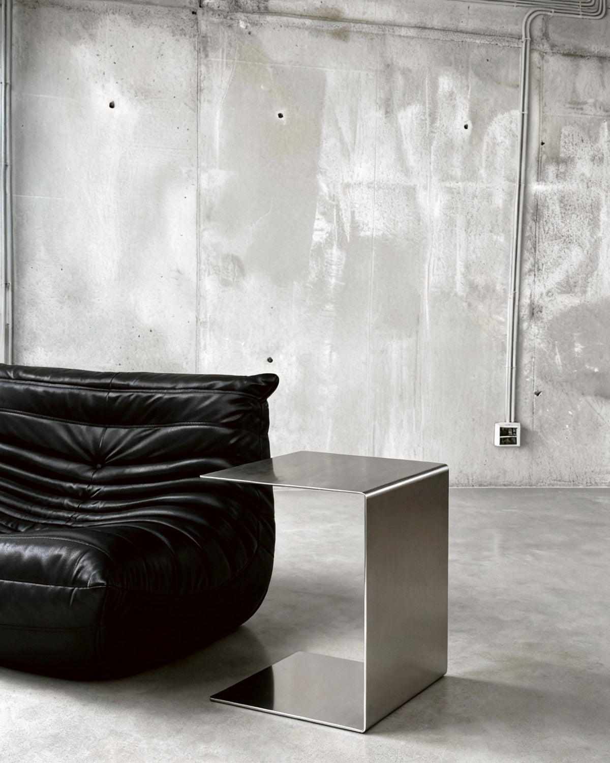 Brushed C vor Betonwand auf Betonboden mit schwarzem lignet rose Sofa aus Leder