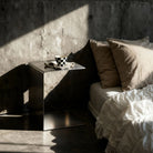 Brushed C  als Nachttisch mit Keramik Kaffeetasse auf Betonboden vor Betonwand neben Bett