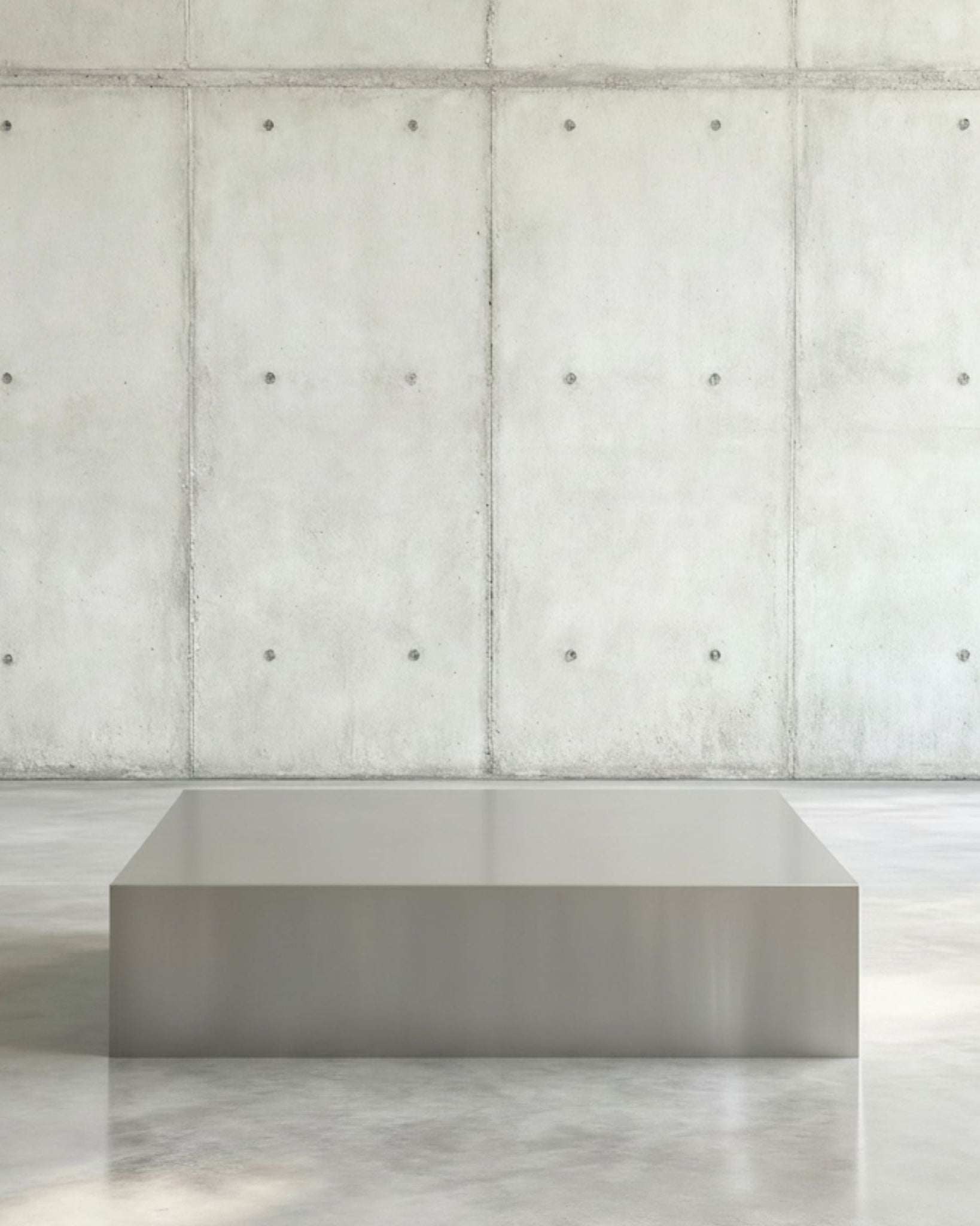 Brushed Q Couchtisch in gebürstetem Edelsthahl auf grauen Betonboden vor grauer Betonwand mit Löchern