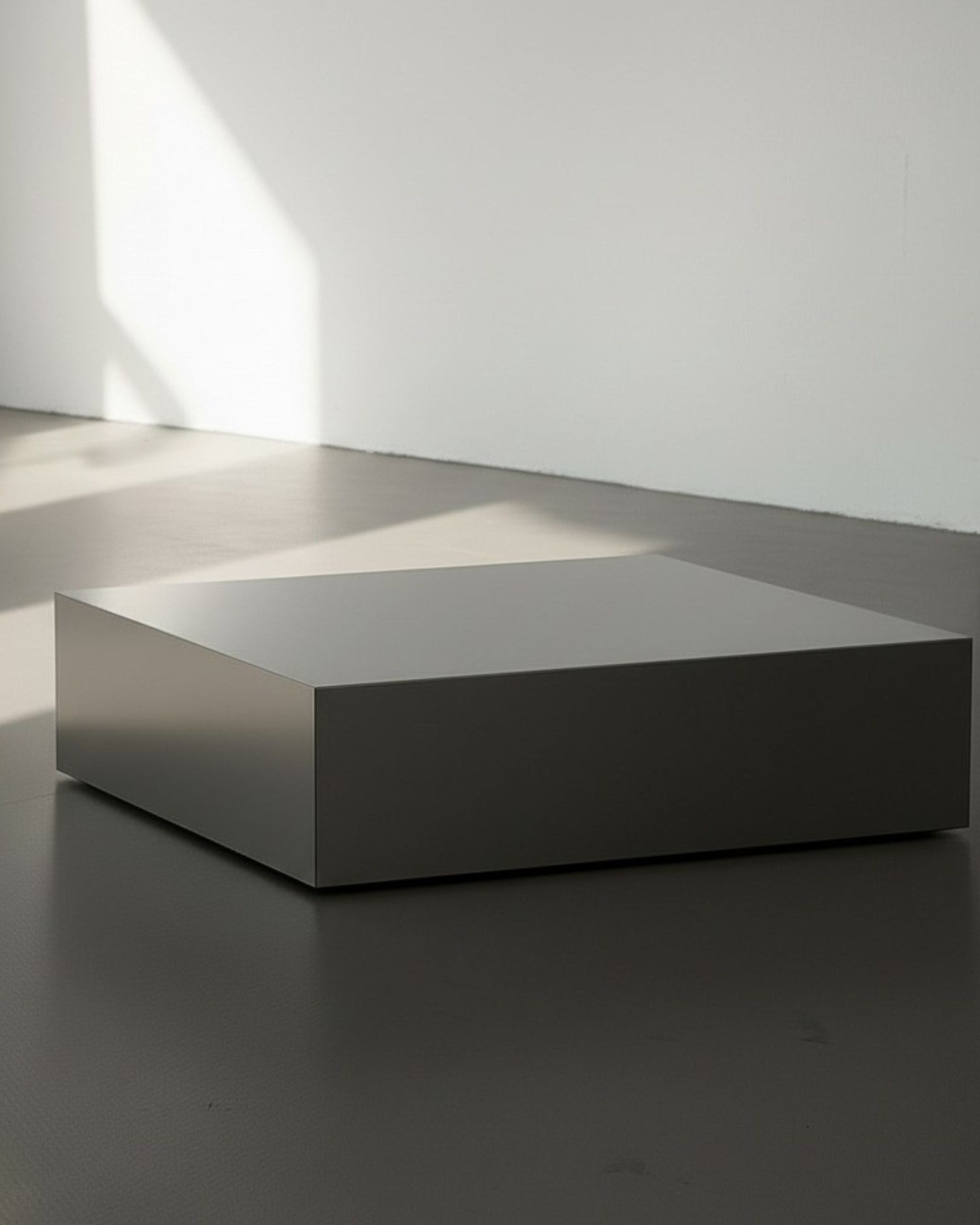 Brushed Q aus gebürstetem Edelstahl auf grauen Betonboden vor weißer Wand und Lichtspiel