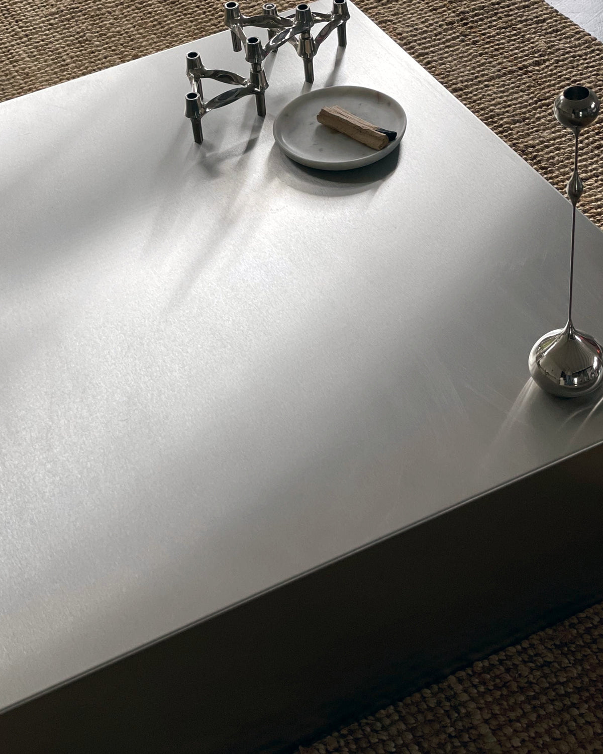 Detailaufnahme eines Couchtischs aus gebürstetem Edelstahl mit stilvoller Dekoration und natürlichem Lichteinfall