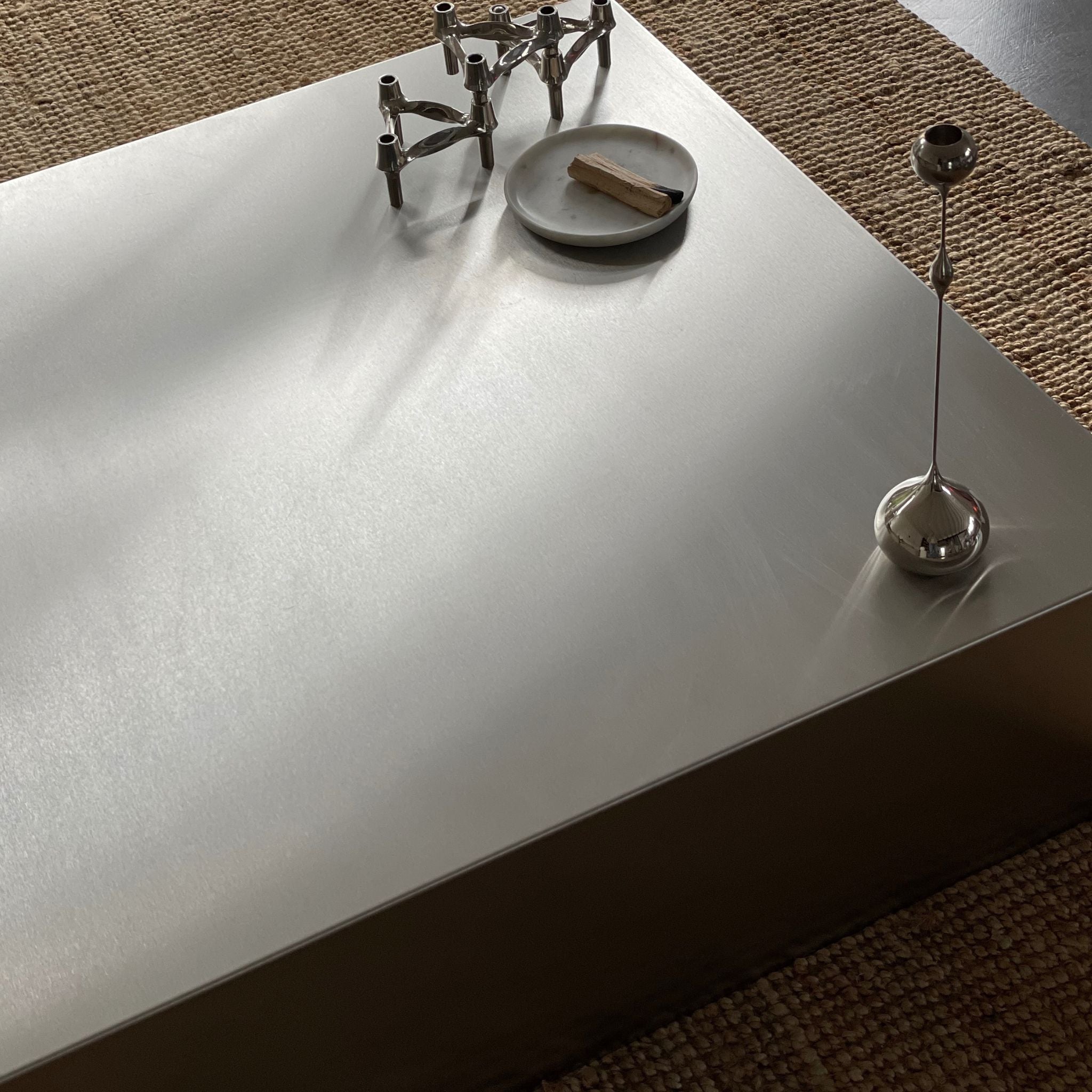 Detailaufnahme eines Couchtischs aus gebürstetem Edelstahl mit stilvoller Dekoration und natürlichem Lichteinfall