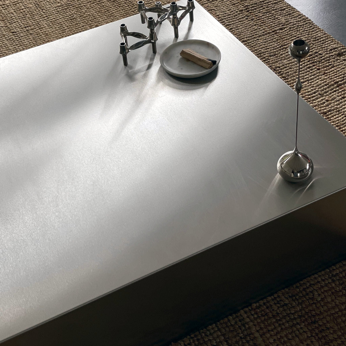 Detailaufnahme eines Couchtischs aus gebürstetem Edelstahl mit stilvoller Dekoration und natürlichem Lichteinfall