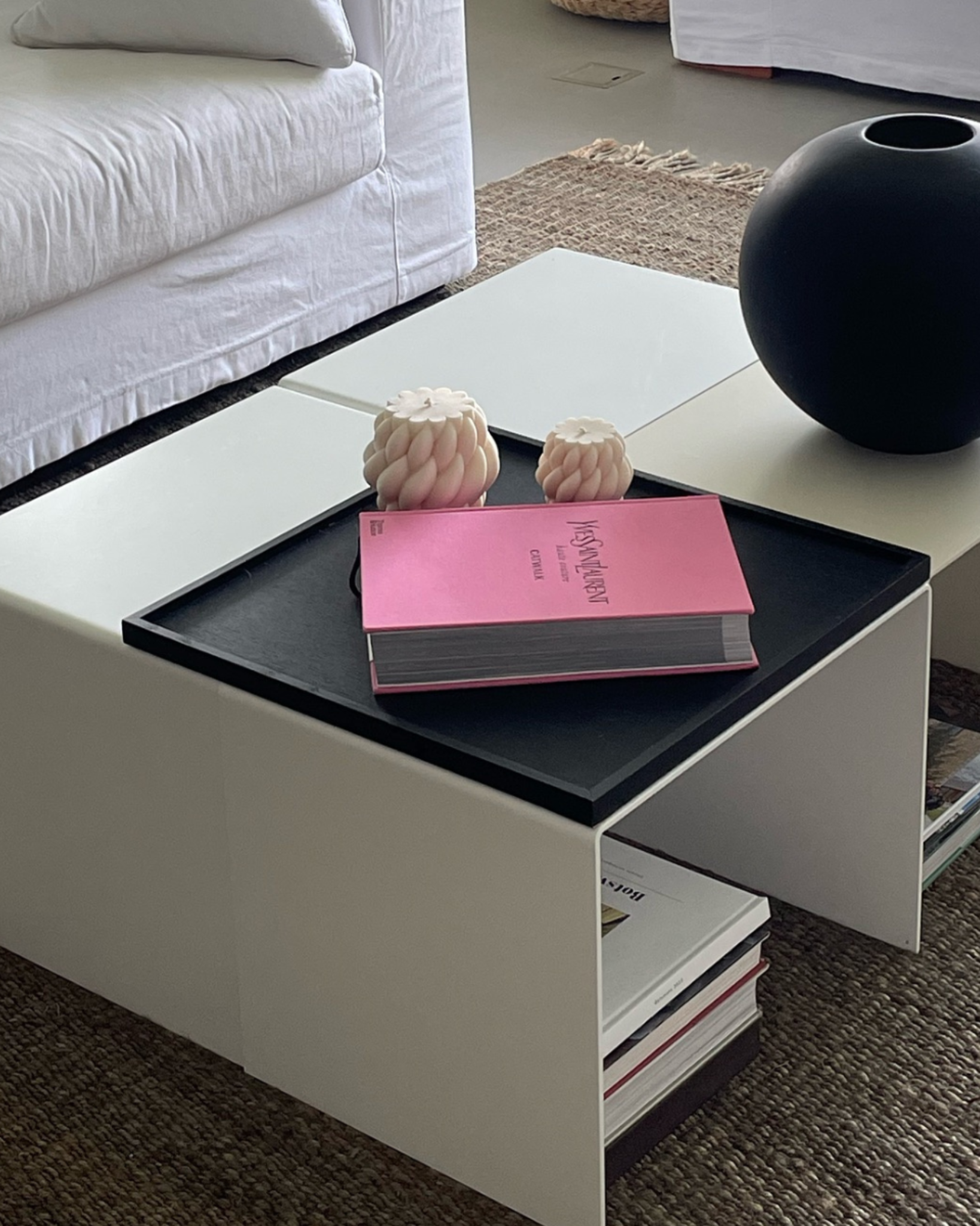 Moderner weißer Couchtisch mit integriertem Regal, dekoriert mit schwarzer Vase, Designbuch und Kerzen in einem stilvollen Wohnzimmer