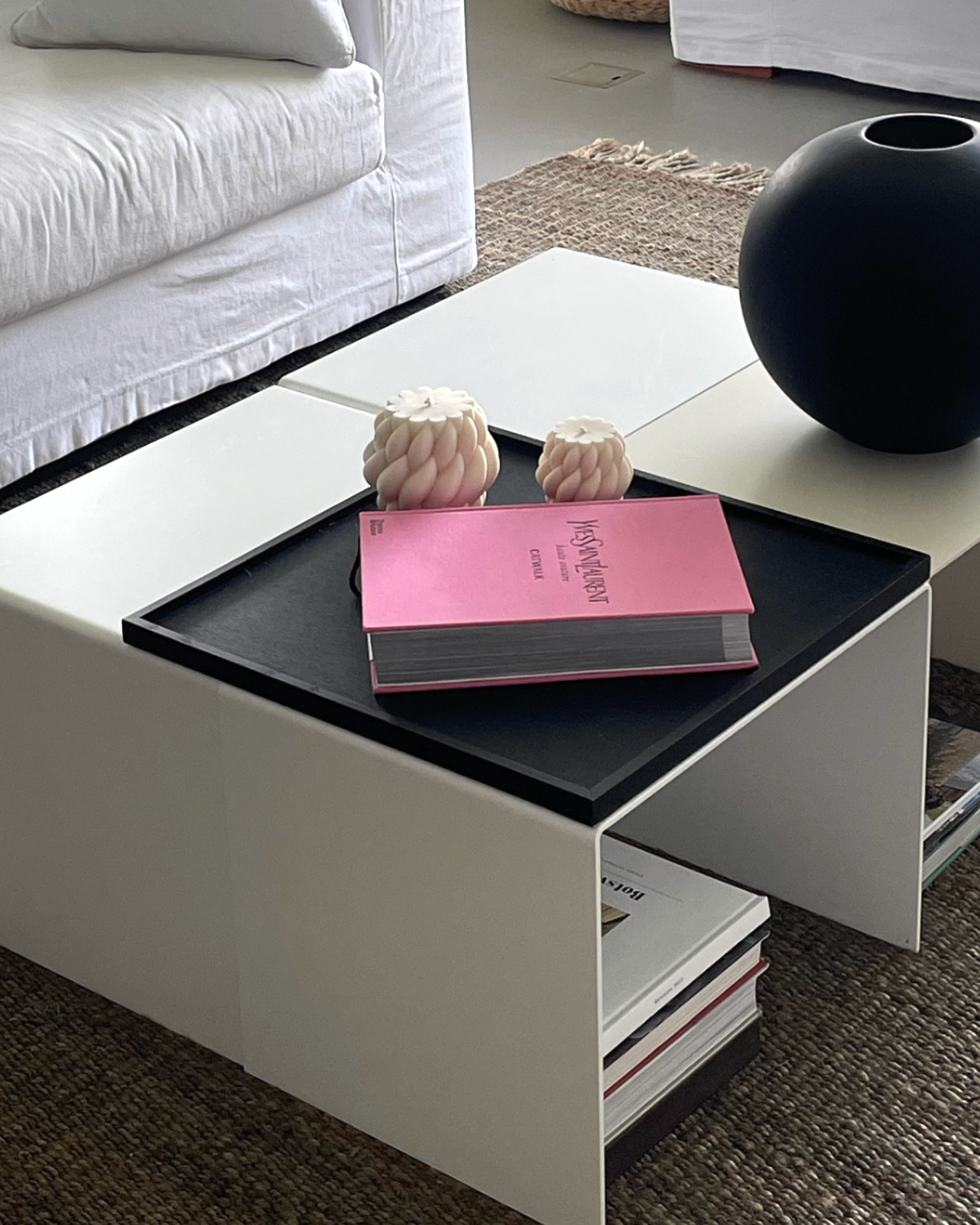 Moderner weißer Couchtisch mit integriertem Regal, dekoriert mit schwarzer Vase, Designbuch und Kerzen in einem stilvollen Wohnzimmer