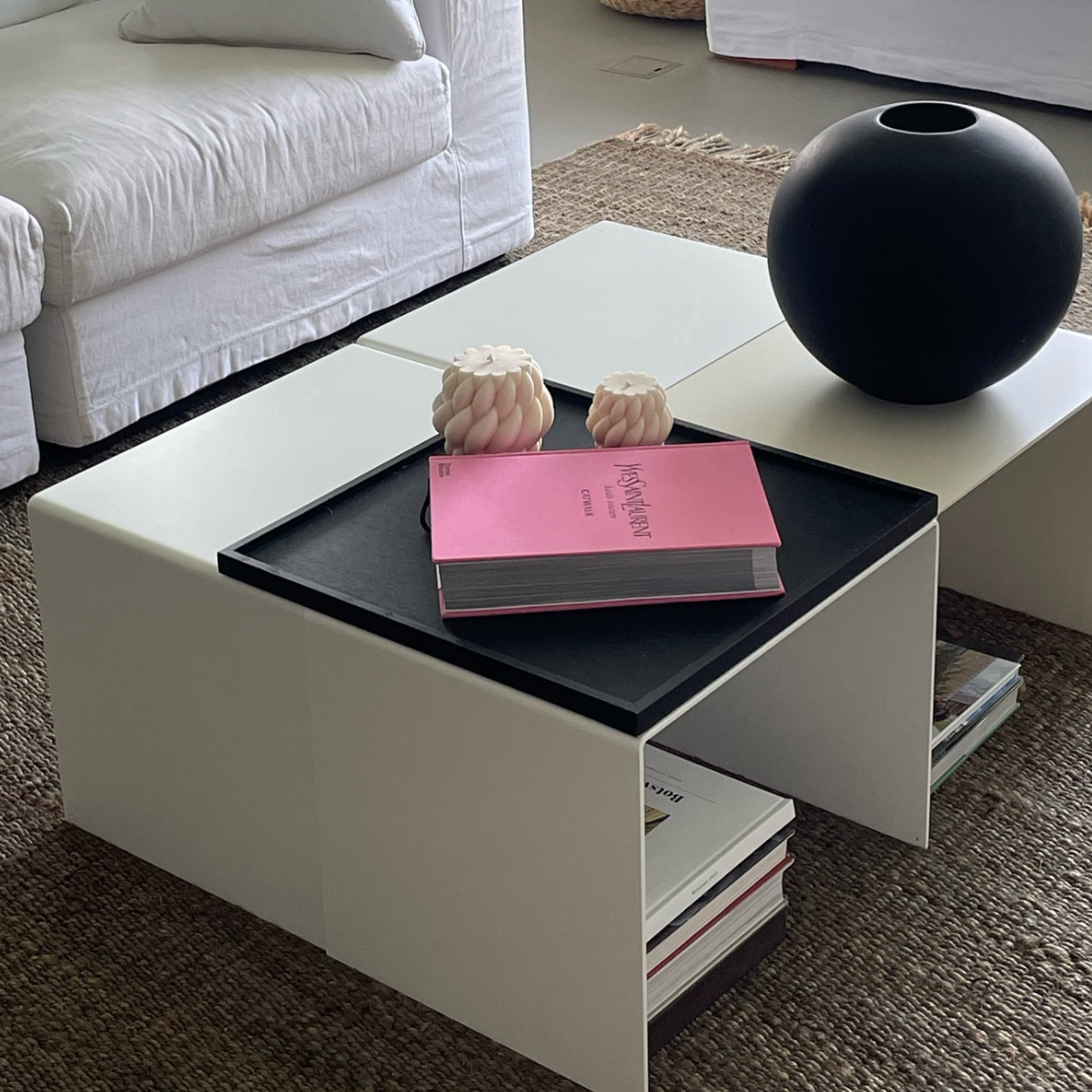 Moderner weißer Couchtisch mit integriertem Regal, dekoriert mit schwarzer Vase, Designbuch und Kerzen in einem stilvollen Wohnzimmer