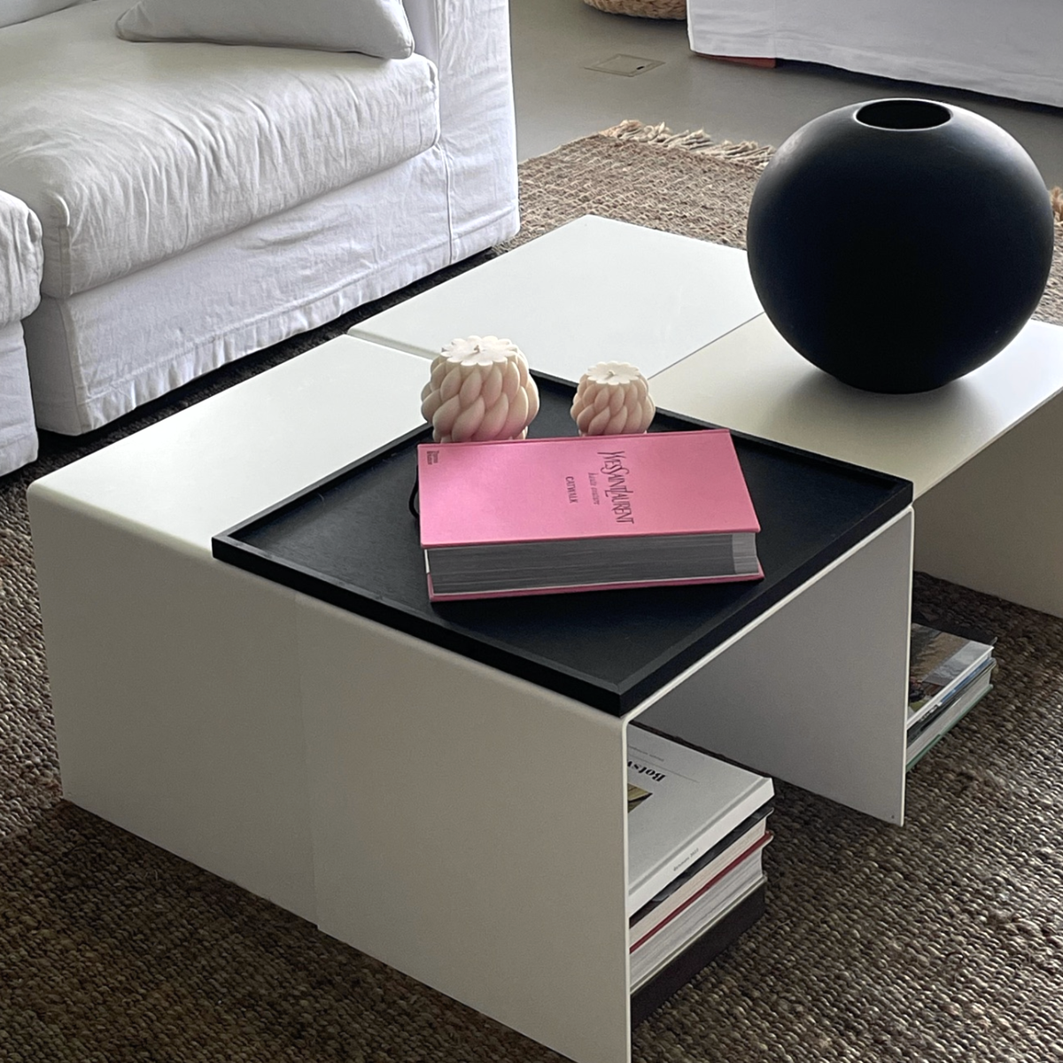 Moderner weißer Couchtisch mit integriertem Regal, dekoriert mit schwarzer Vase, Designbuch und Kerzen in einem stilvollen Wohnzimmer