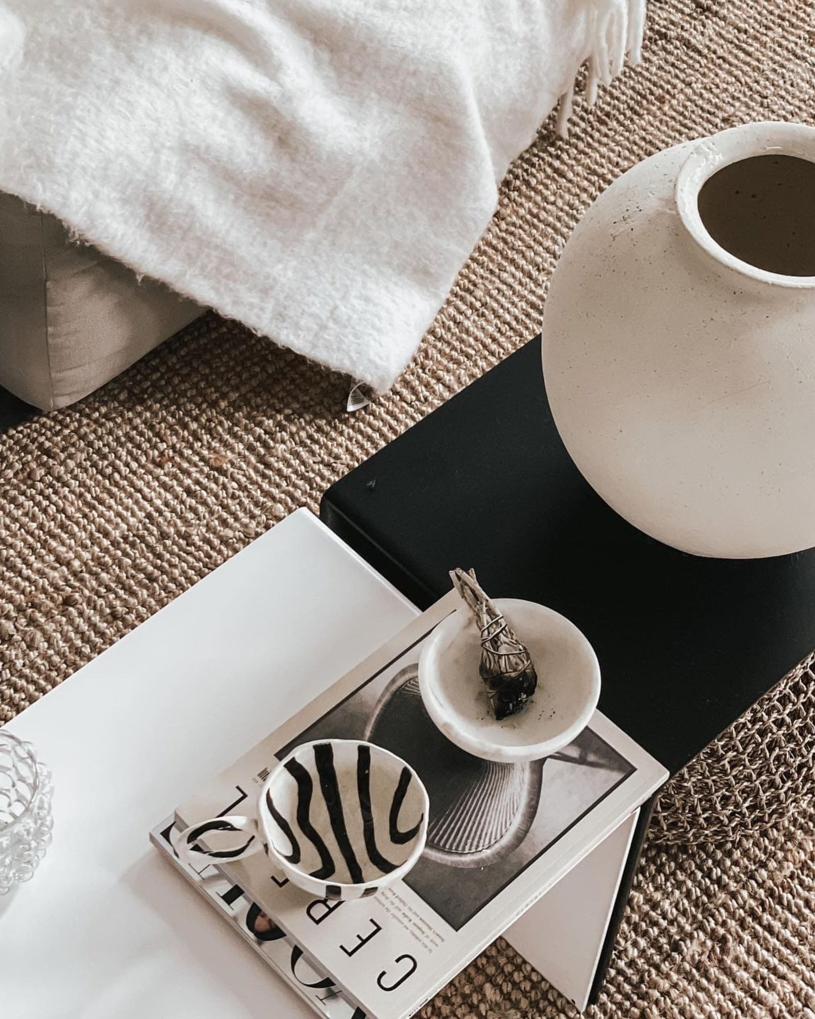 Weiße und schwarze Couchtisch-Kombination mit Keramikvase, Magazinen und Schalen auf geflochtenem Teppich