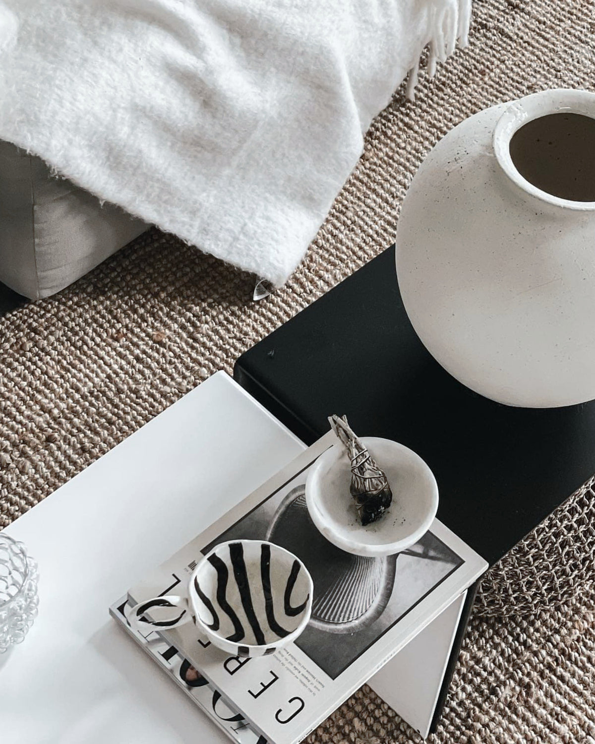 Weiße und schwarze Couchtisch-Kombination mit Keramikvase, Magazinen und Schalen auf geflochtenem Teppich