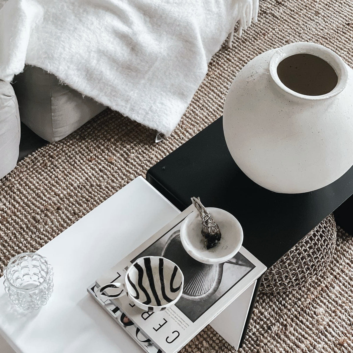 Weiße und schwarze Couchtisch-Kombination mit Keramikvase, Magazinen und Schalen auf geflochtenem Teppich