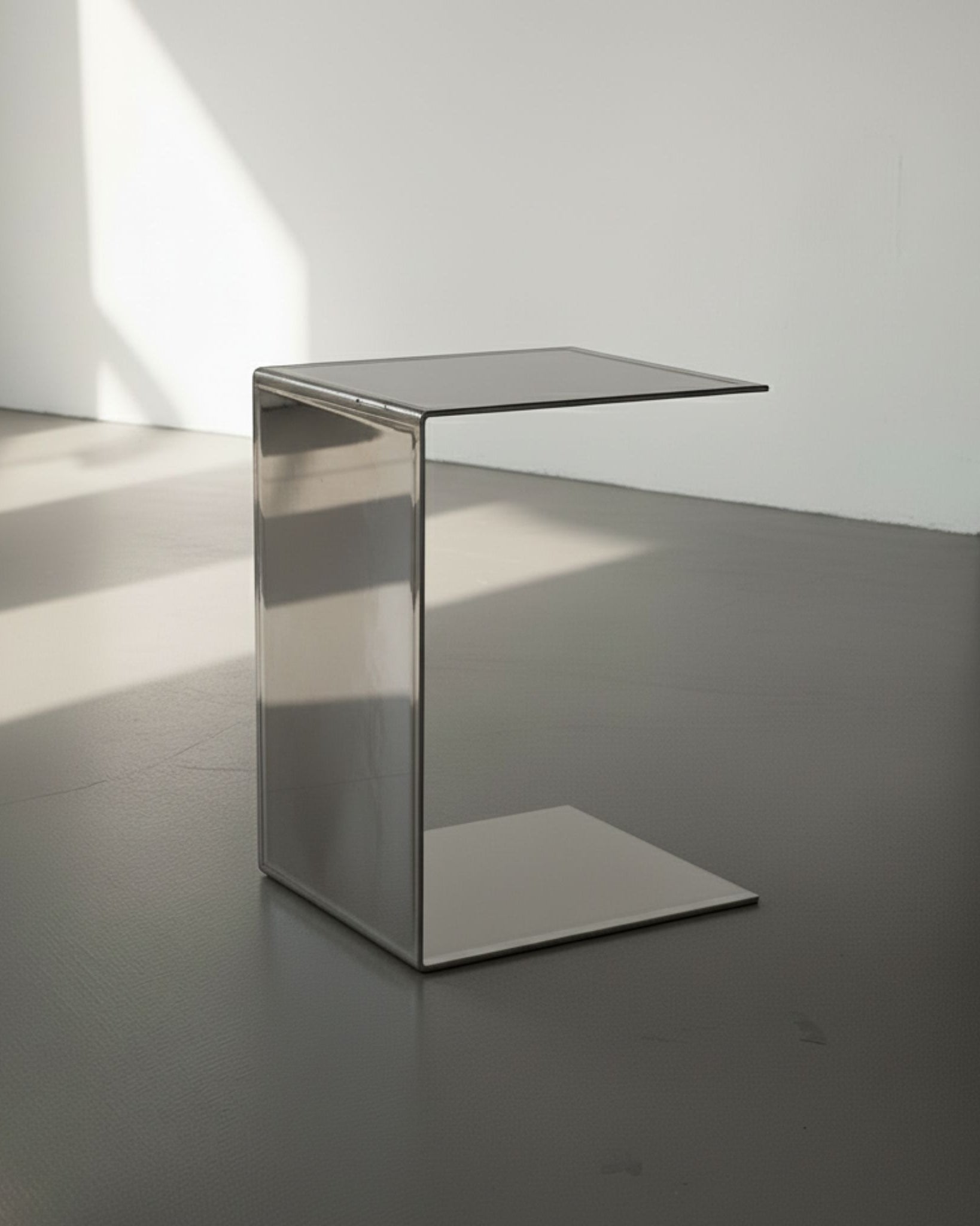 Mirror aus spiegelpoliertem Edelstahl auf grauen Betonboden vor weißer Wand und Lichtspiel