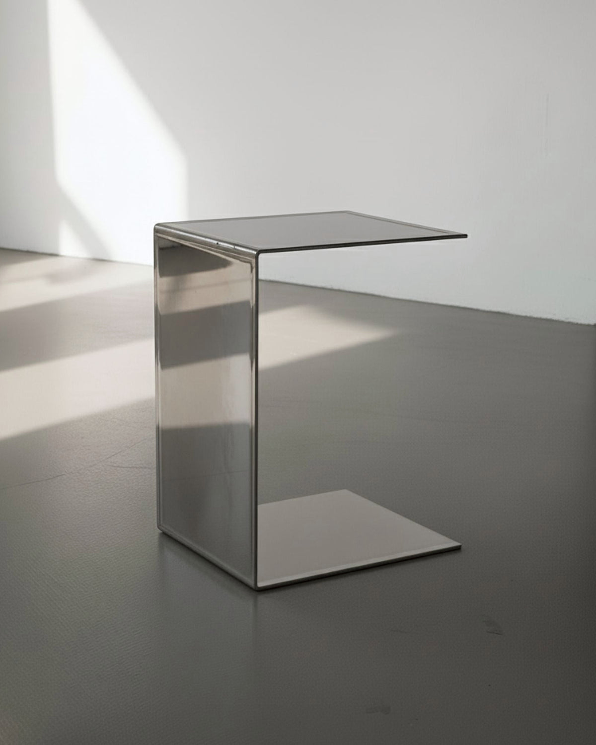 Mirror aus spiegelpoliertem Edelstahl auf grauen Betonboden vor weißer Wand und Lichtspiel