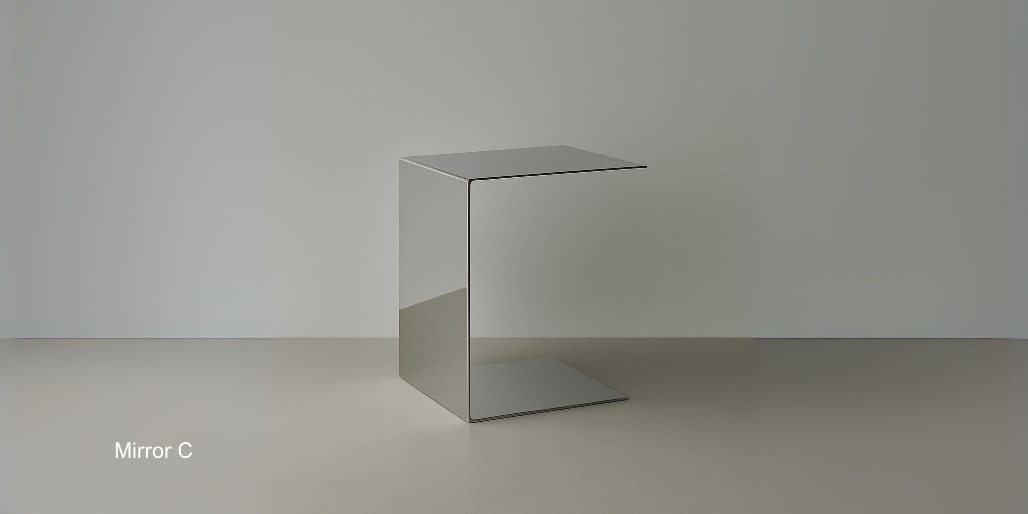 Beistelltisch Mirror C aus spiegelpoliertem Edelstahl im minimalistischen C-Design auf hellem Boden vor grauer Wand