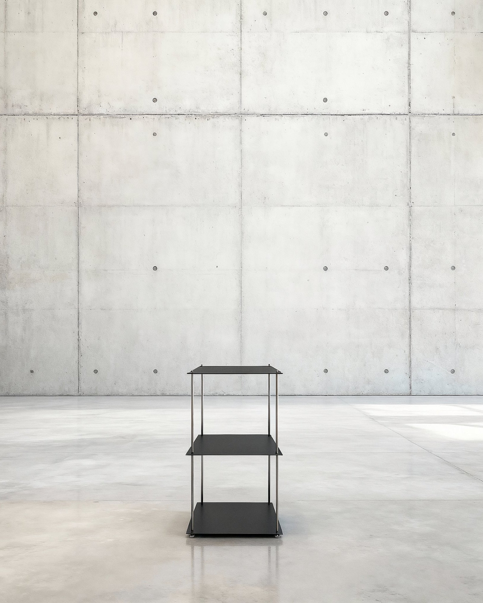 Modulum mit 3 Fachböden in schwarz ultramatt auf grauen Betonboden vor grauer Betonwand mit Löchern