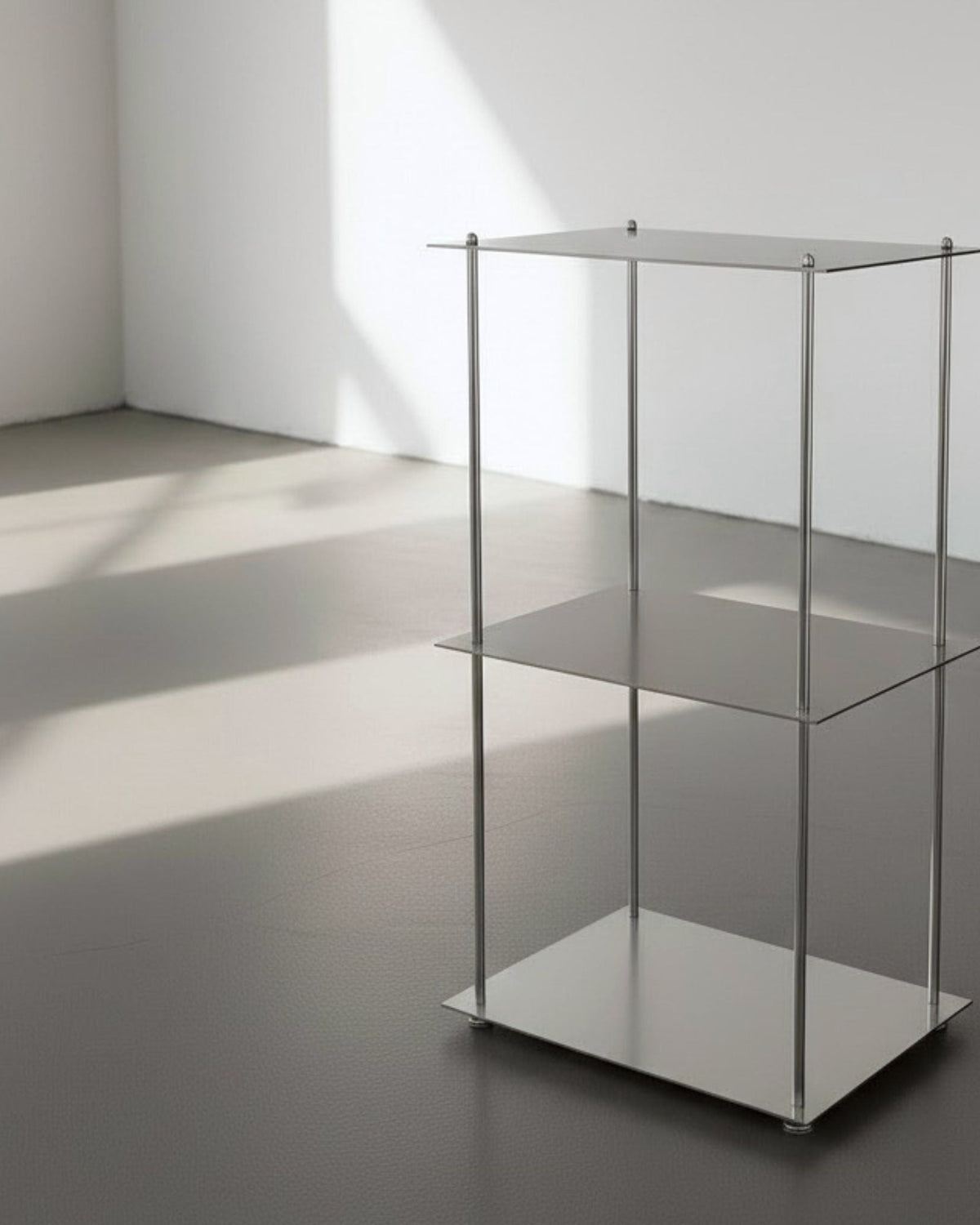 Modulum mit 3 Fachböden aus gebürstetem Edelstahl auf grauen Betonboden vor weißer Wand und Lichtspiel