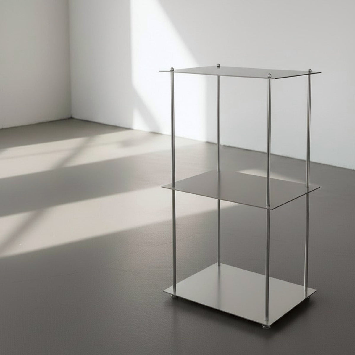 Modulum mit 3 Fachböden aus gebürstetem Edelstahl auf grauen Betonboden vor weißer Wand und Lichtspiel