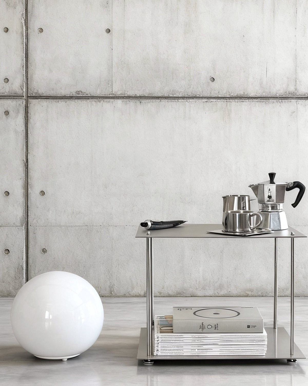 Modulum Regalsystem aus Edelstahl mit Kaffeeset und Magazinen in modernem Betonraum mit minimalistischer Kugellampe